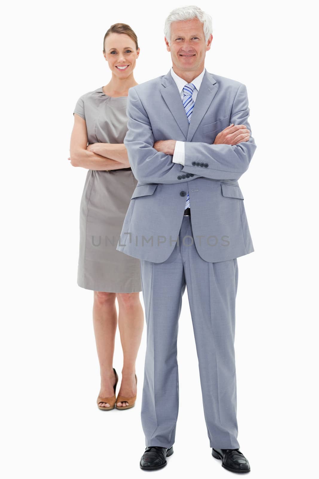 White hair businessman with a woman in background smiling and crossing their arms against white background