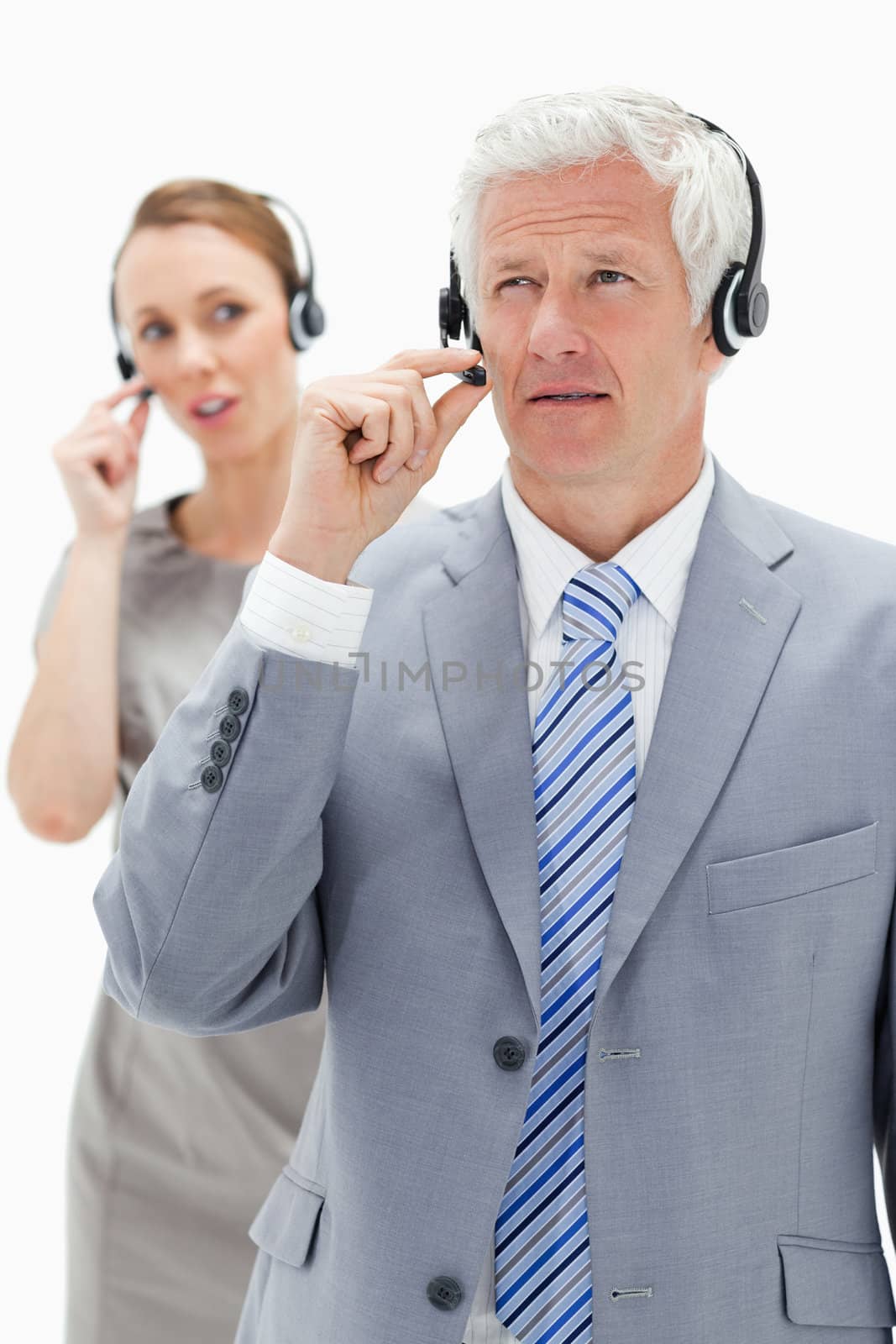 Close-up of a white hair businessman with a woman talking in background while wearing headset against white background