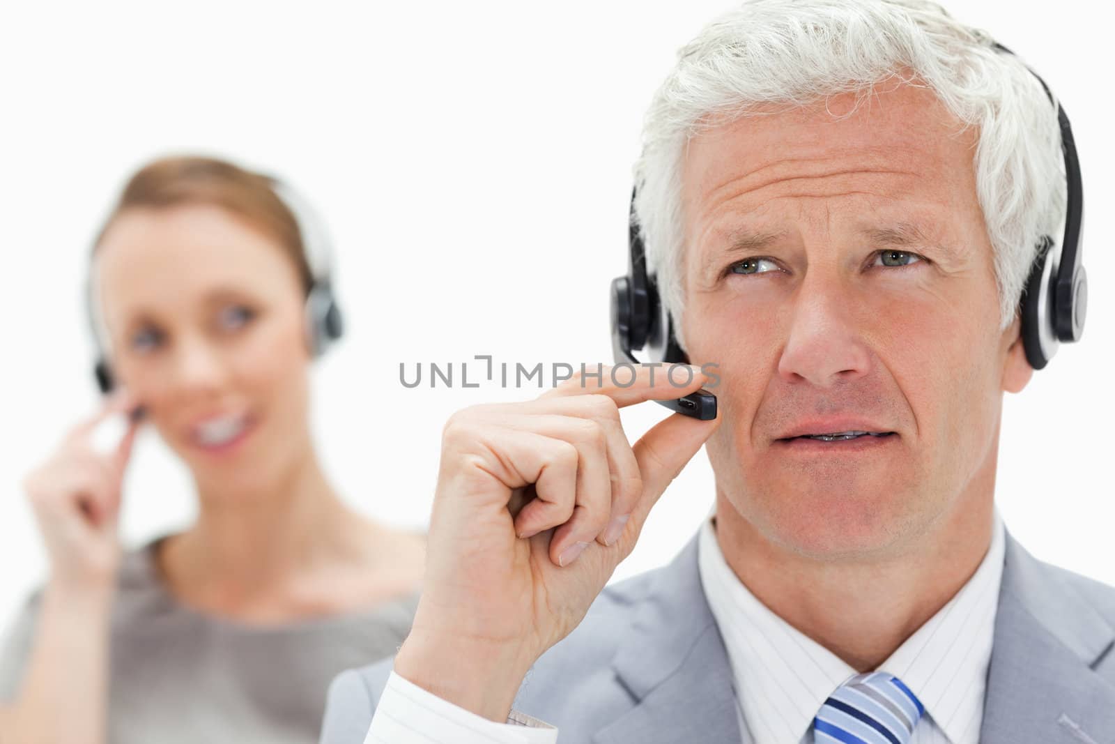 Close-up of a white hair man with a woman talking in background while wearing a headset against white background