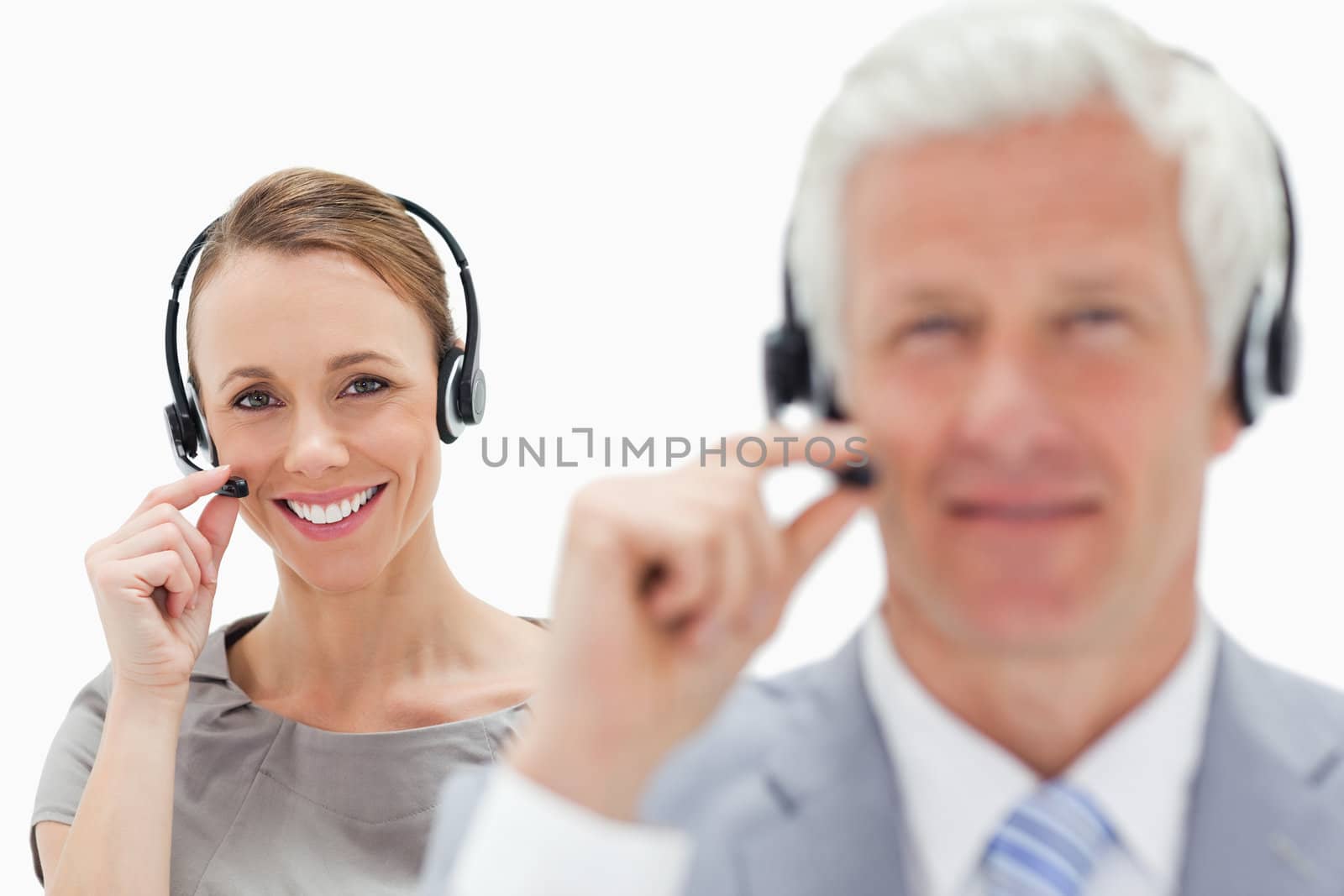 Close-up of a smiling woman talking in background with a white hair man while wearing a headset against white background