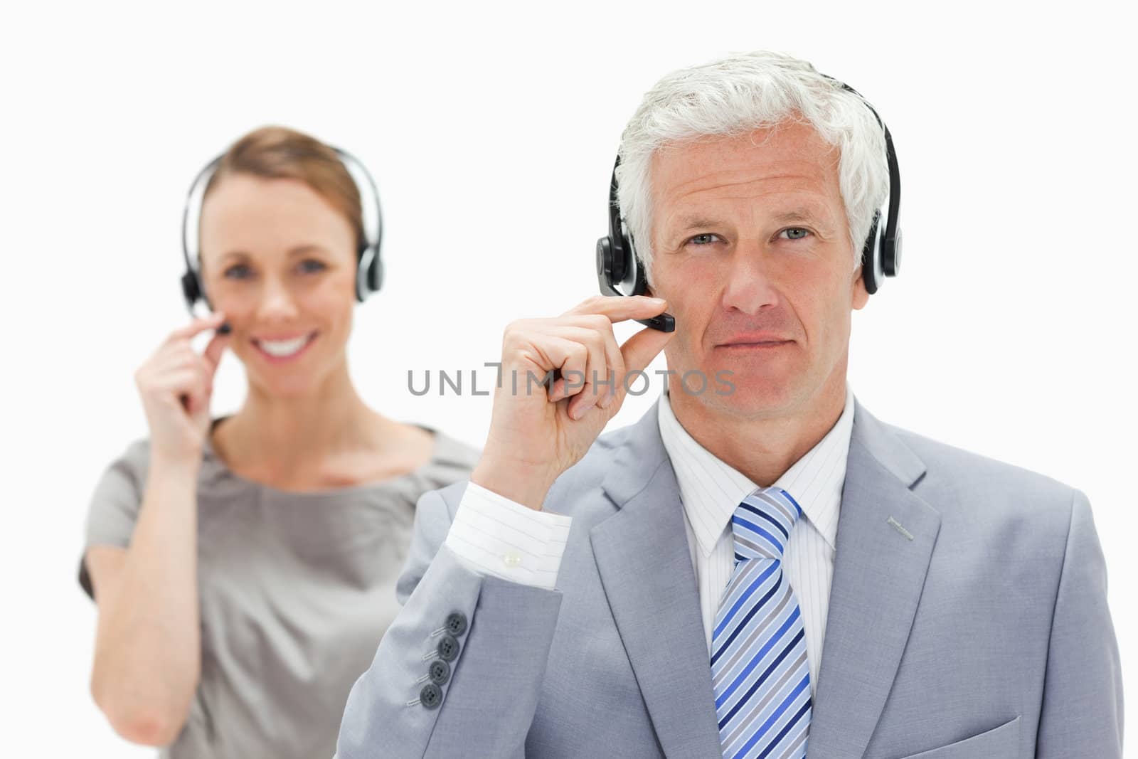 Close-up of a white hair man with a smiling woman in background wearing a headset against white background