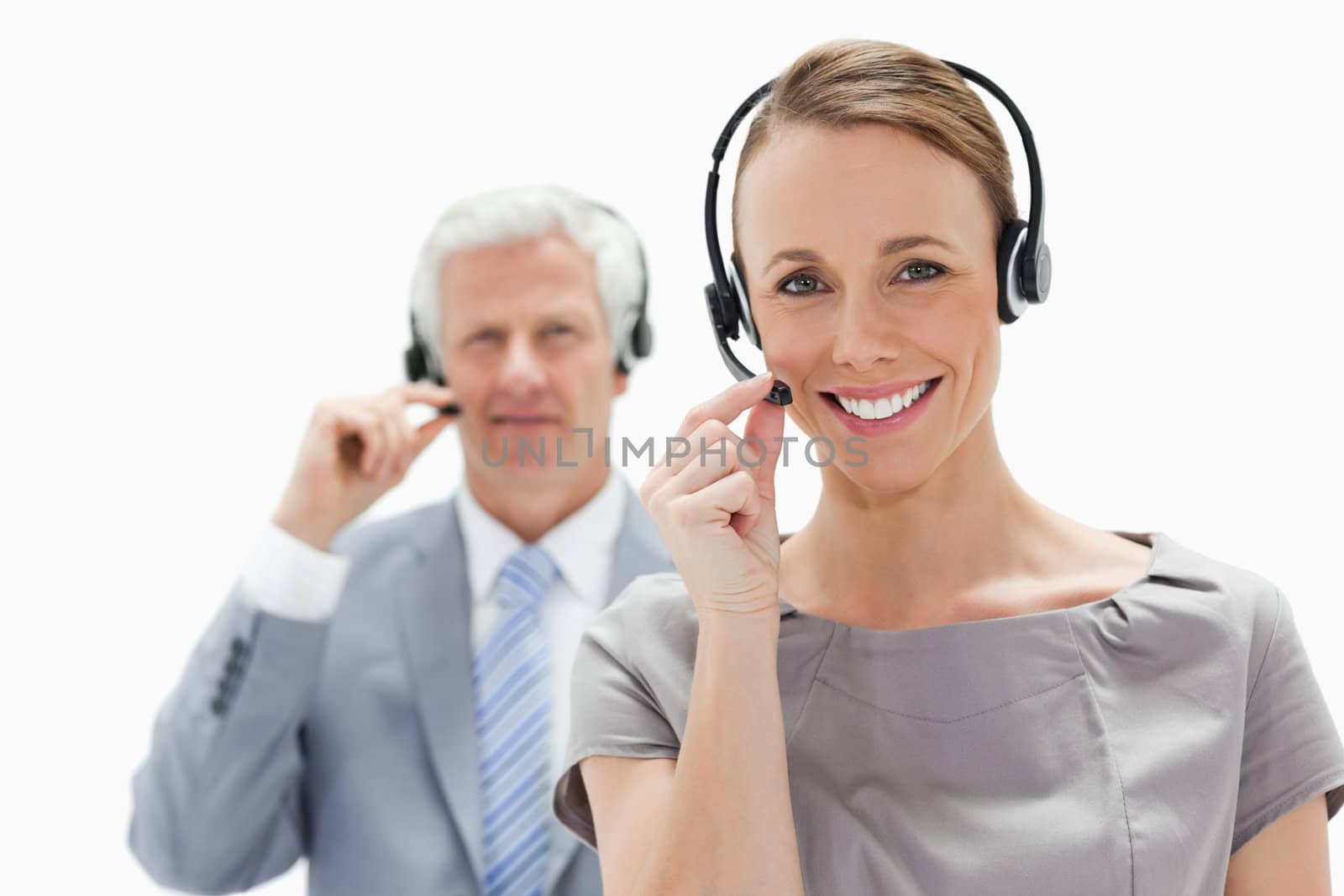 Close-up of a smiling woman wearing a headset with a white hair businessman in background