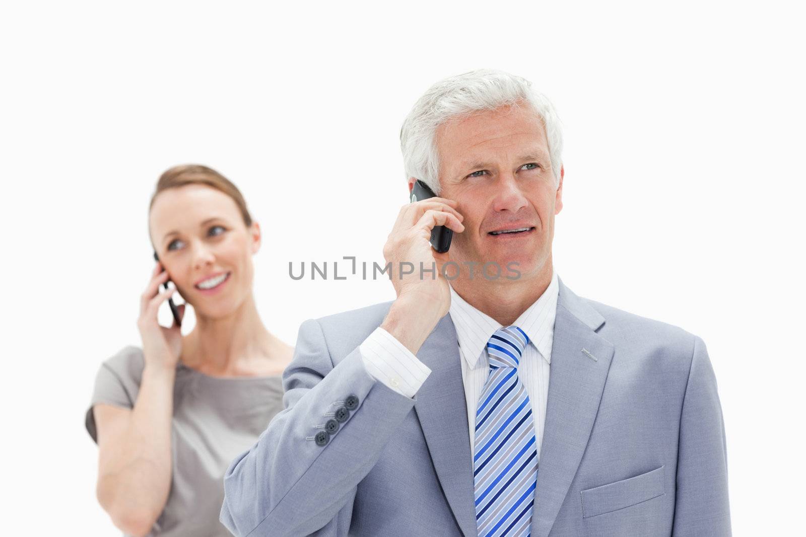 Close-up of a white man hair man dressed in a suit talking on the phone with a smiling woman in background