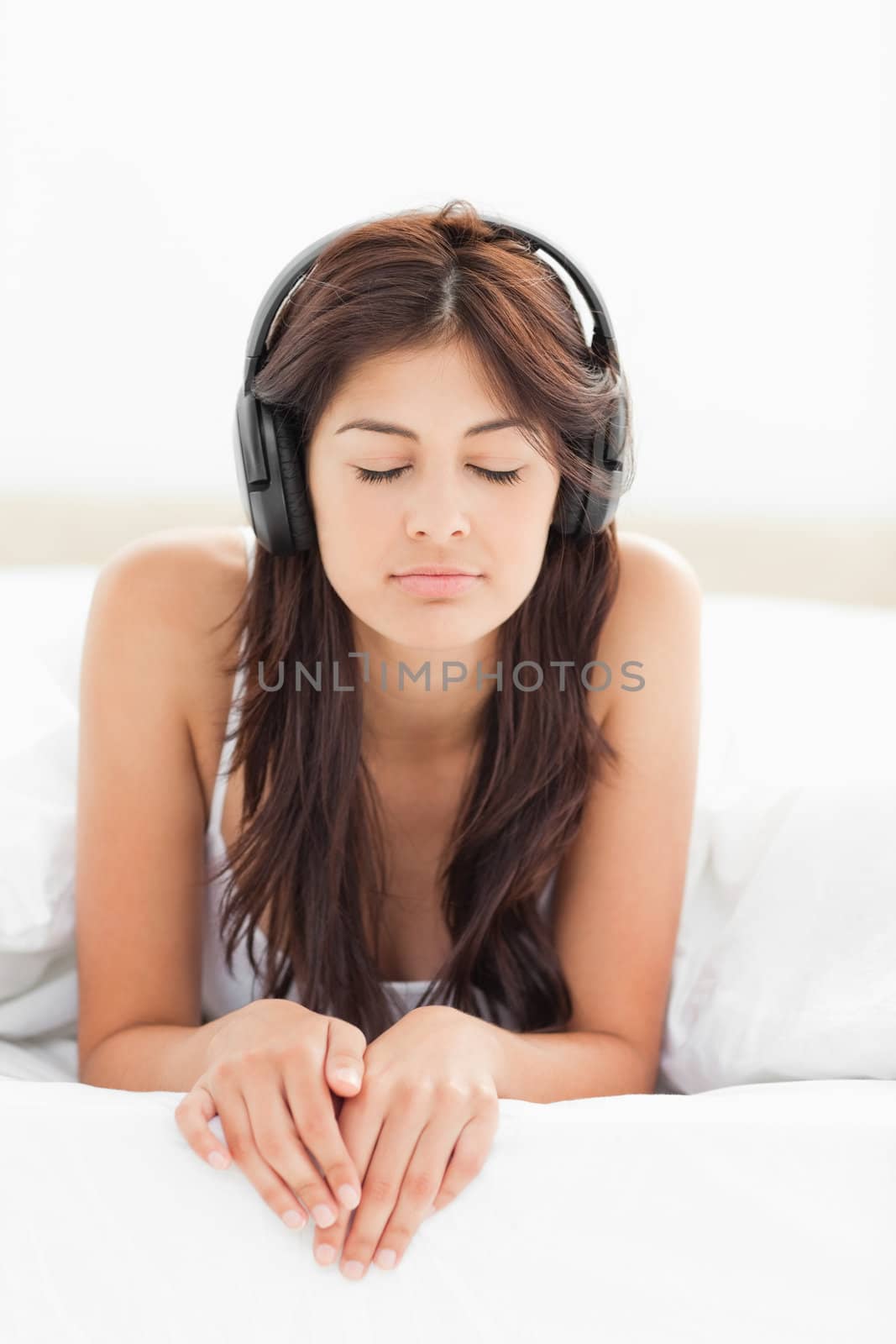 A woman with headphones on listening to music, her eyes closed and her fingers over the lip of the bed.