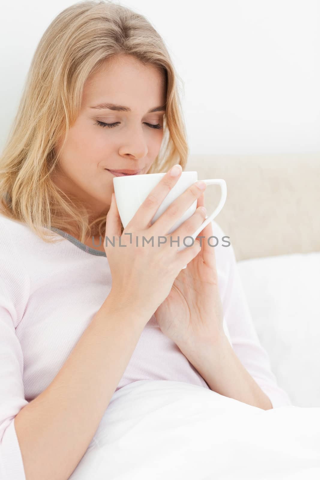 A close up shot of a woman holding a cup up to her face, with her eyes closed. Smelling the contents of the cup.