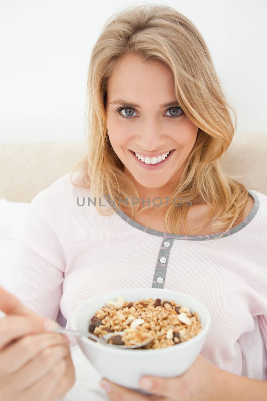 A close shot of a woman about to take a spoon of cereal from the bowl, while looking forward and smiling.