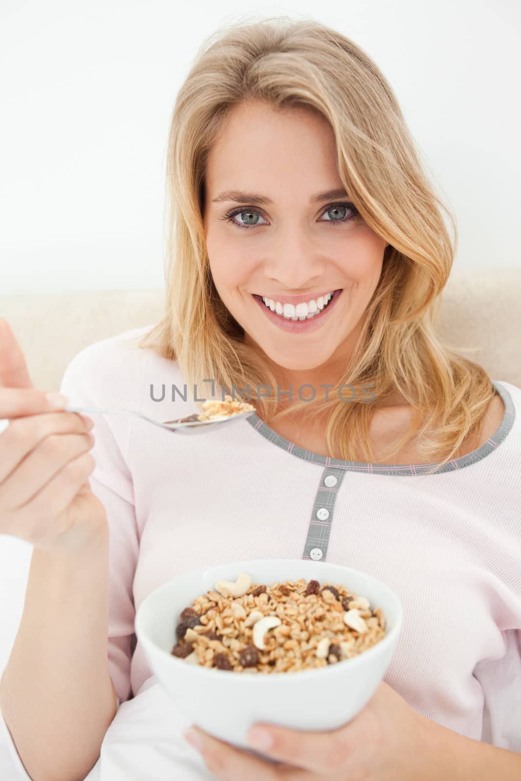 A close up shot of a smiling woman as she has a raised spoon of cereal in her hand.
