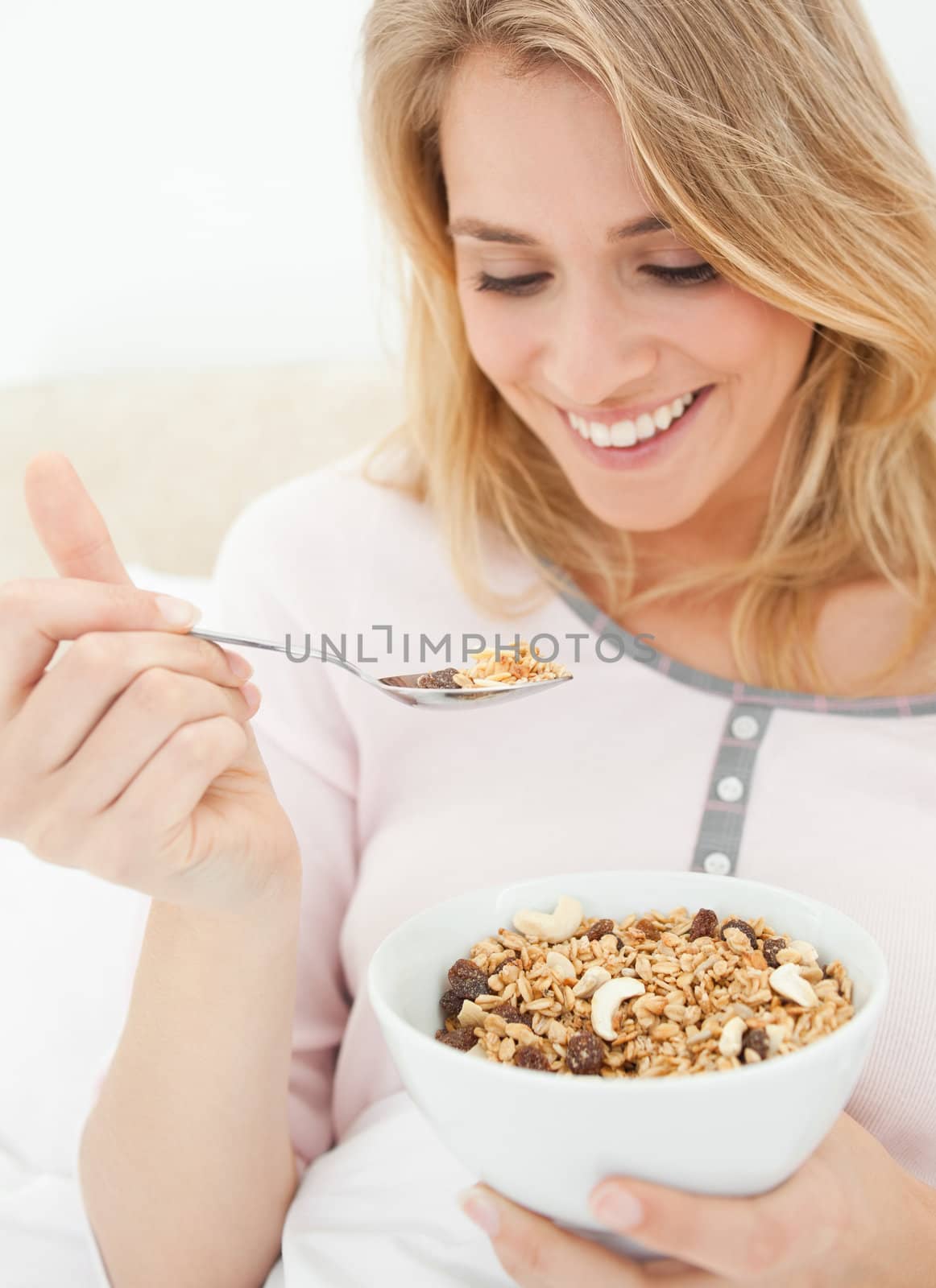 A close up shot of a woman holding a bowl of cereal and a raised spoon of cereal near to her mouth.