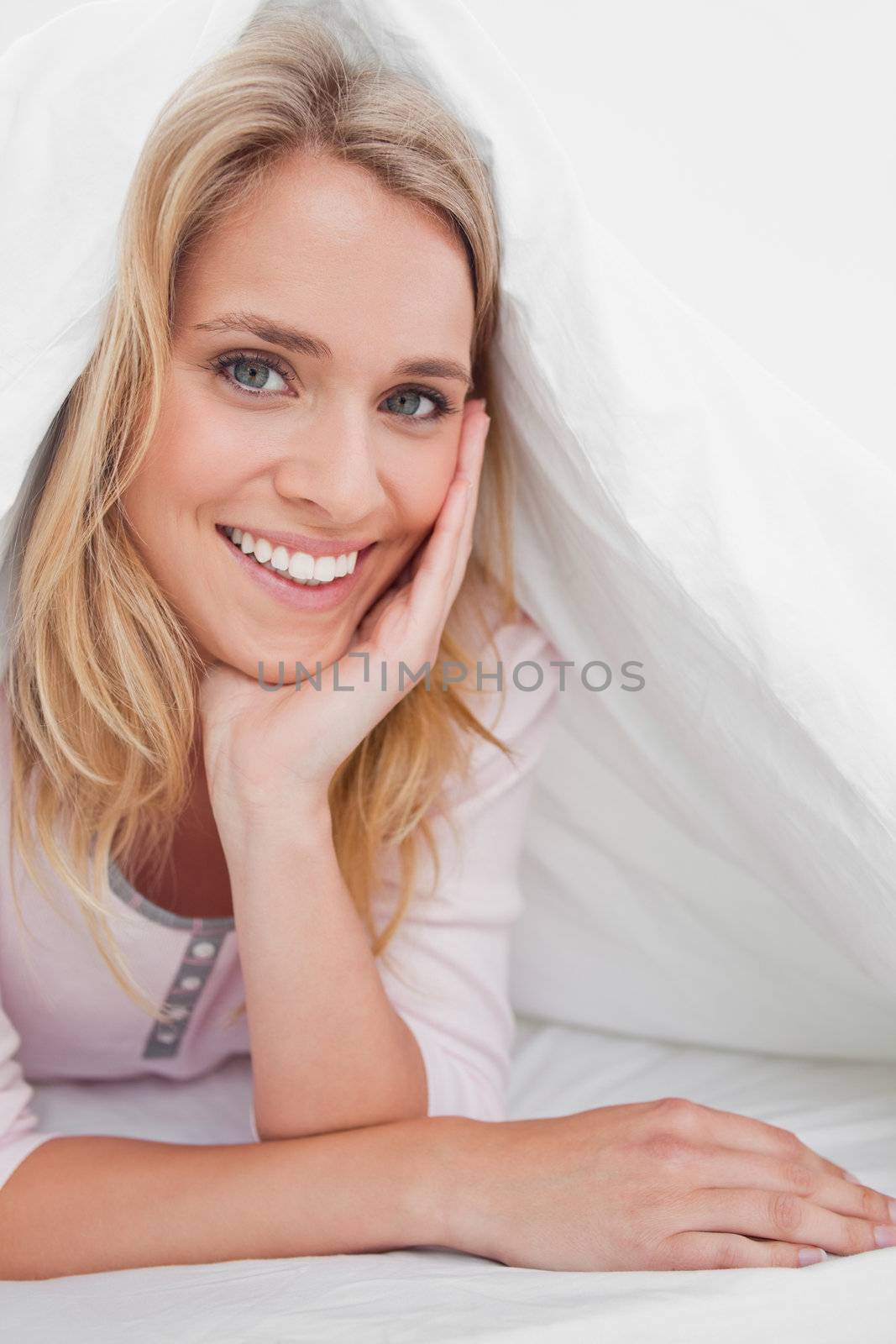 A close up shot of a woman under a quilt with her head being supported by her hand as she smiles.