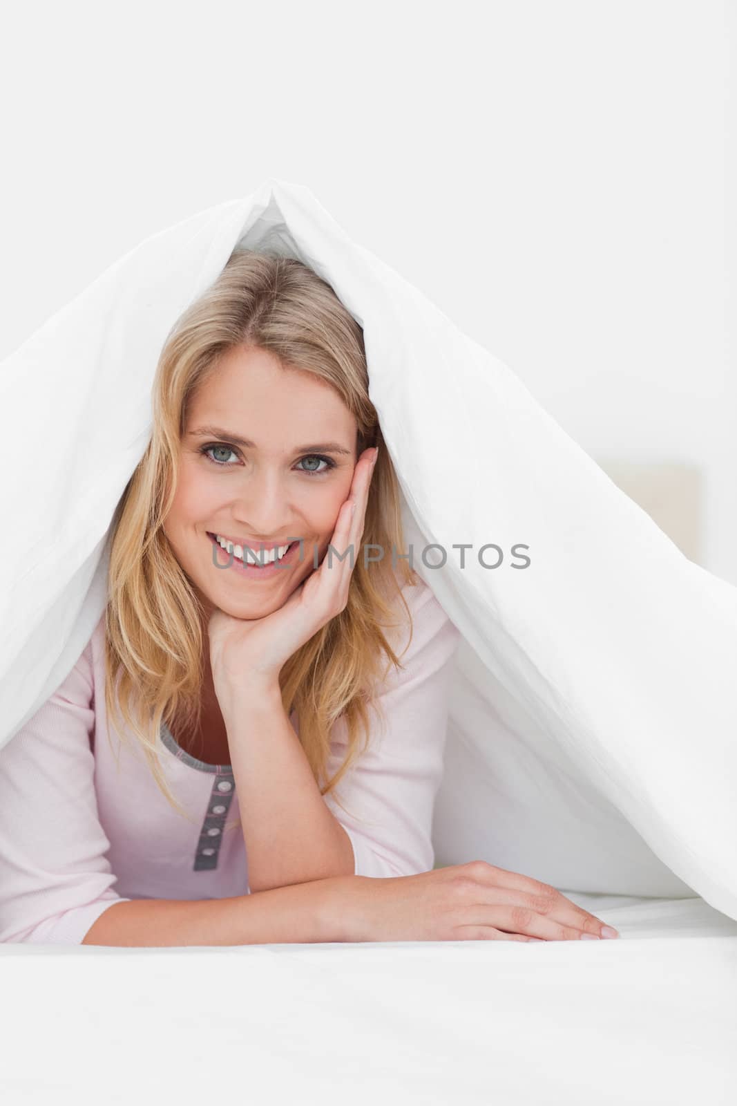 A close up shot of a woman smiling as she lies under a quilt with her hand supporting her head.