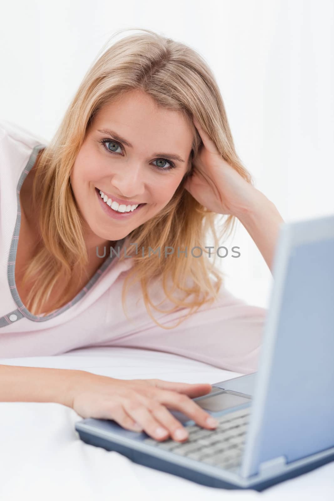 A close up shot of a woman lying on her bed, with her laptop beside her.