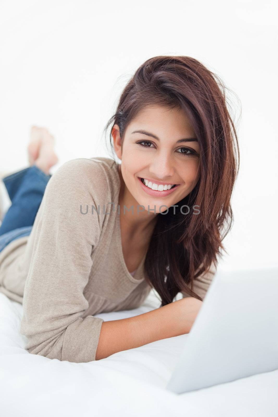 A smiling woman looks in front of her as she smiles, with her tablet on the bed with her.