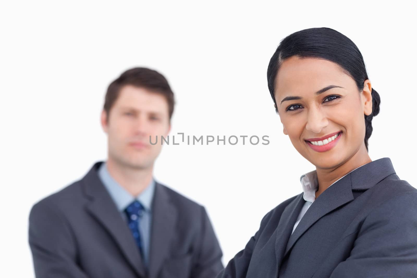 Close up of smiling saleswoman with co-worker behind her against a white background