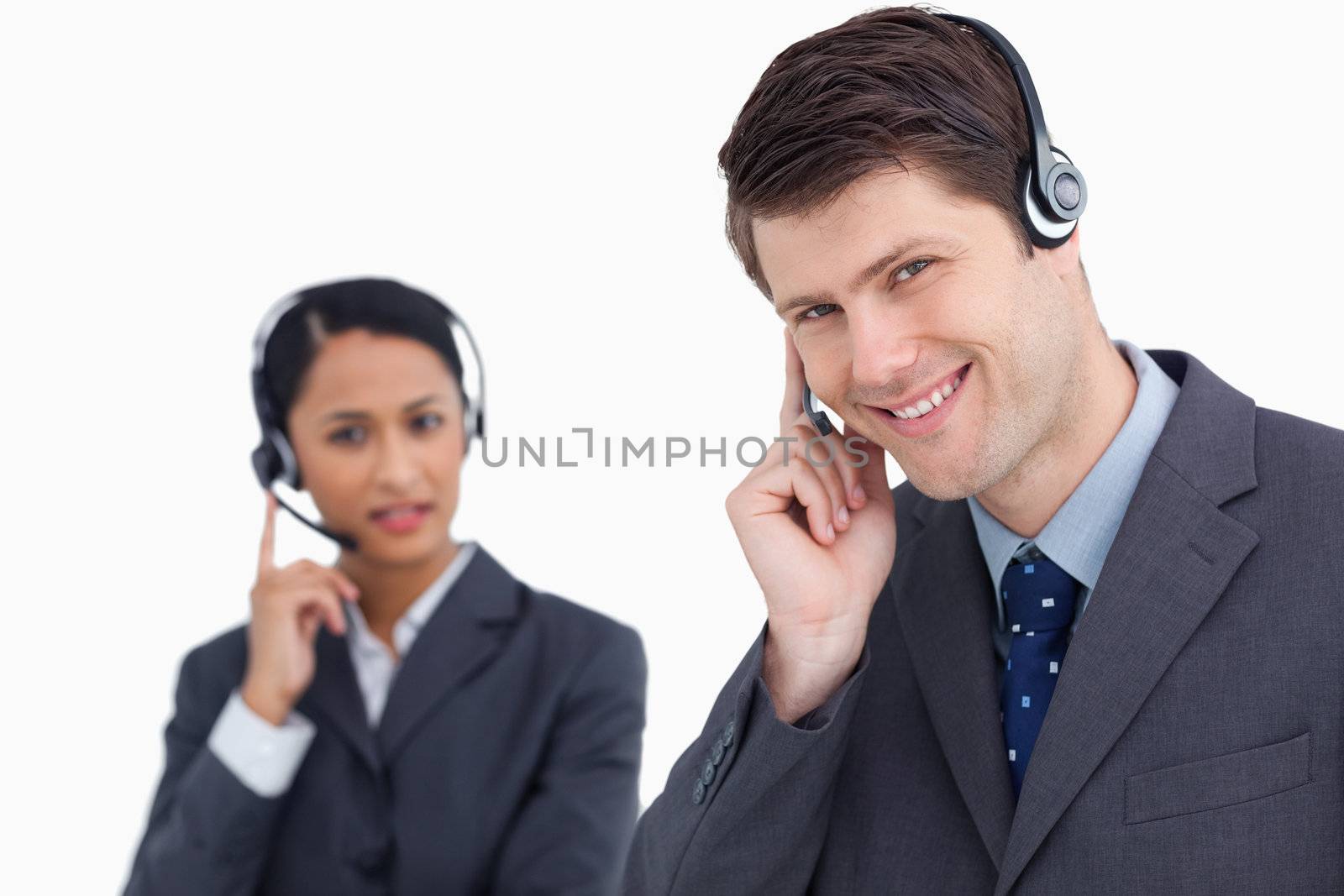 Close up of smiling call center agent with co-worker behind him against a white background