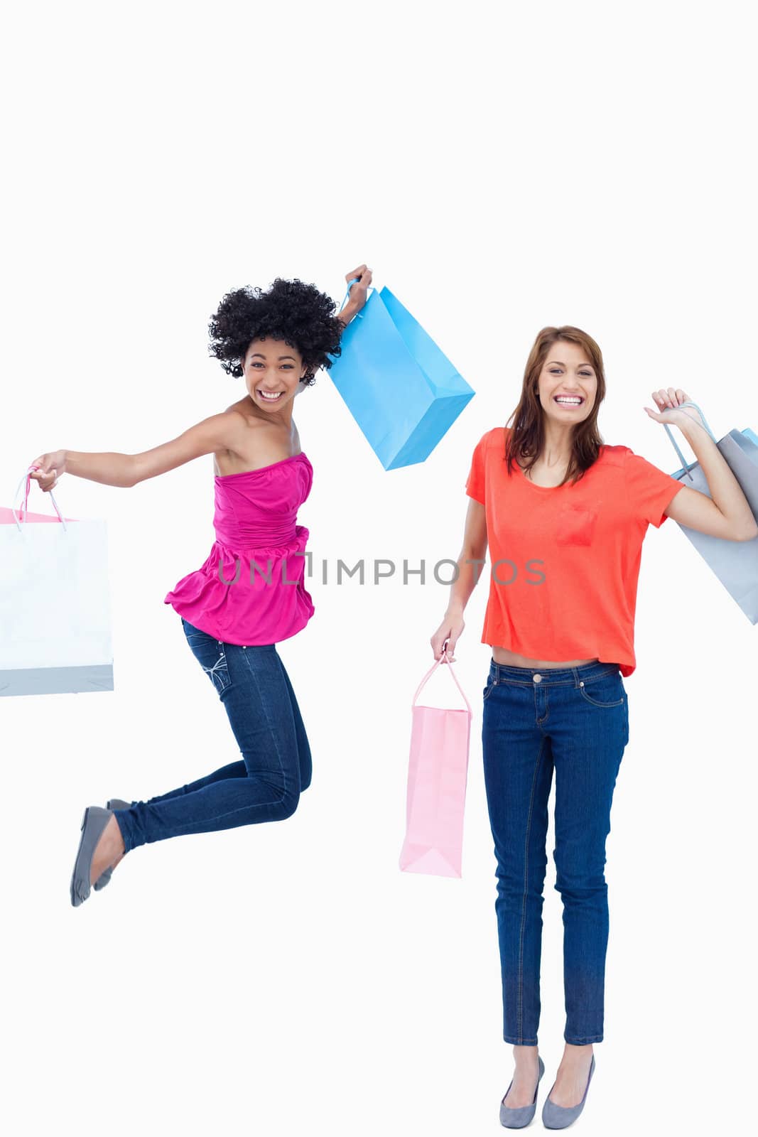 A teenage girl leaping while holding her shopping bags while her friend is smiling