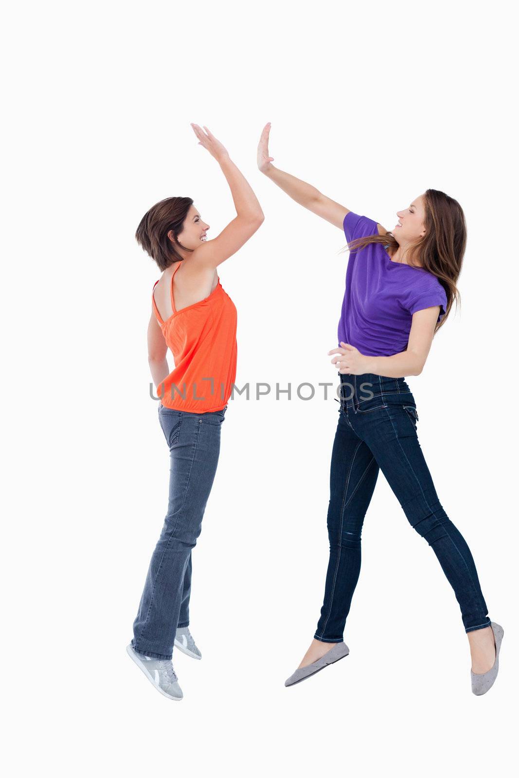 Smiling teenagers jumping while trying to high-five each other in the air