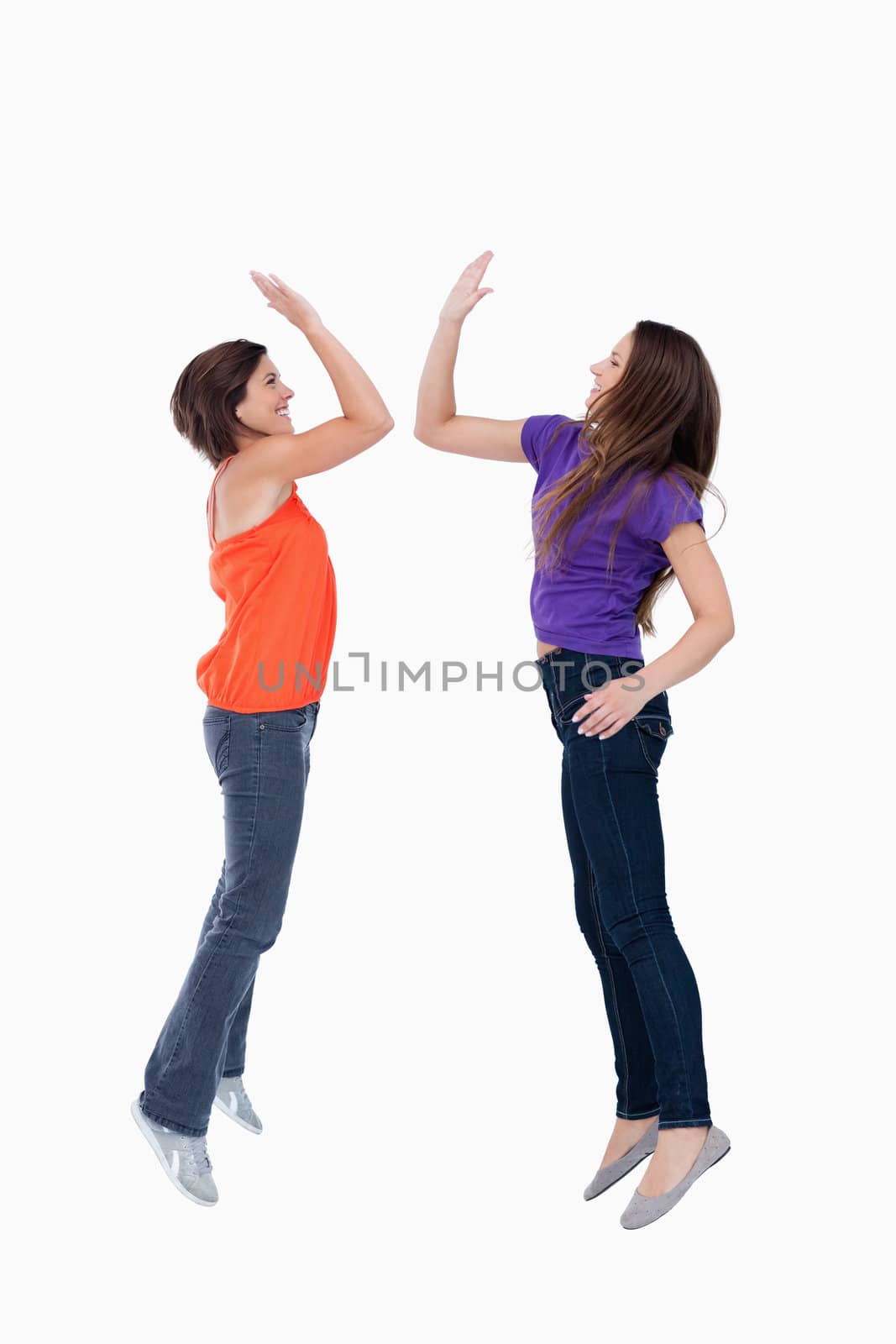 Two teenagers leaping while giving a high-five in the air