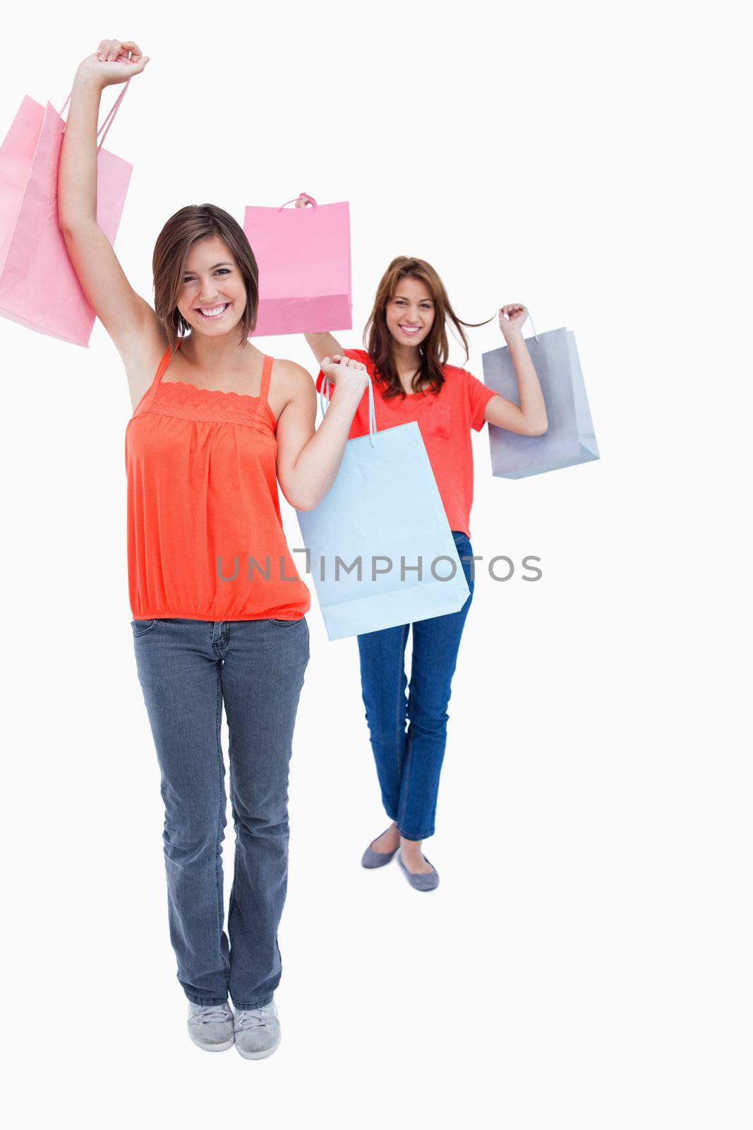 Smiling teenagers holding purchase bags in the air while a friend is behind her