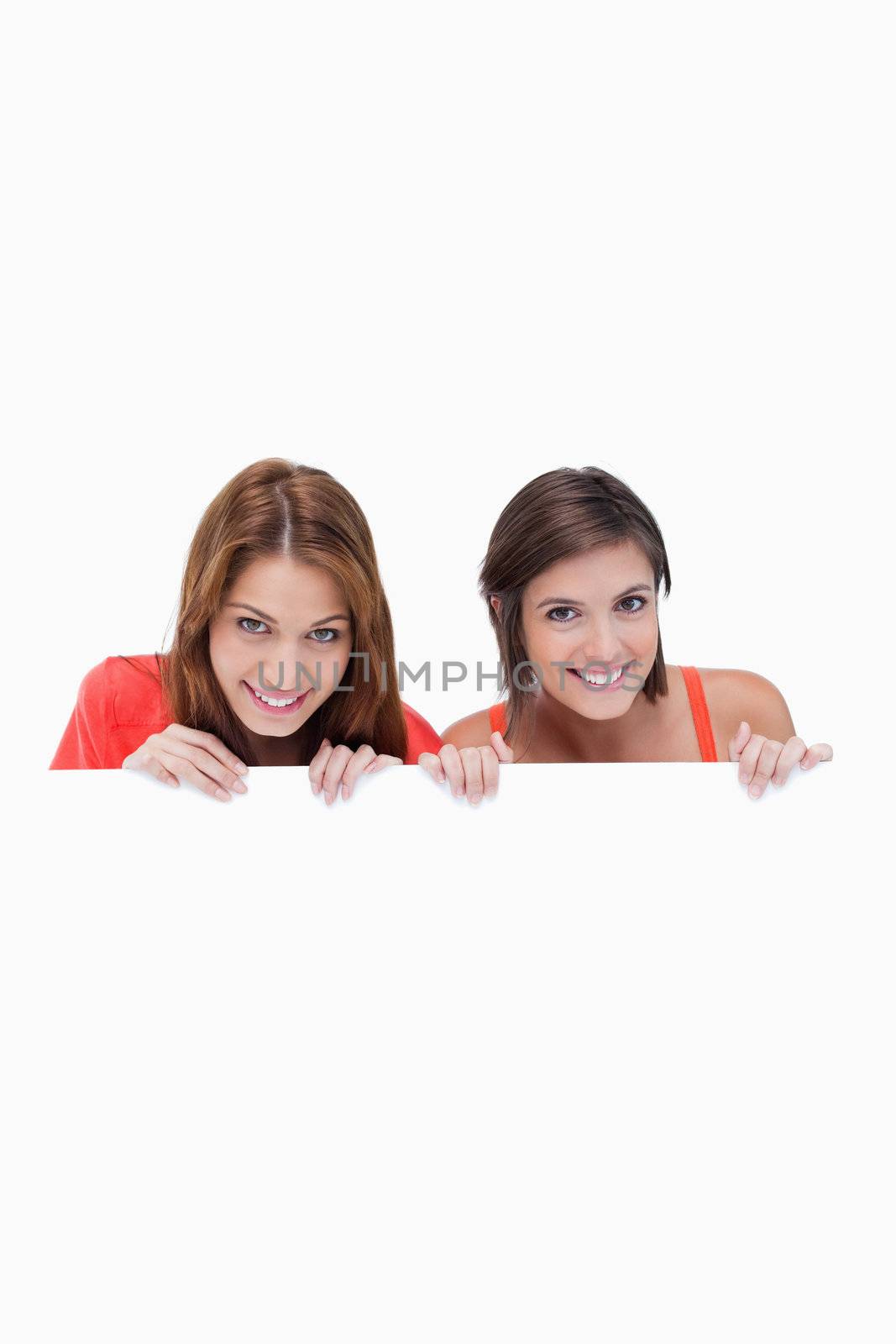 Teenage girls smiling while holding a blank poster and hiding be by Wavebreakmedia