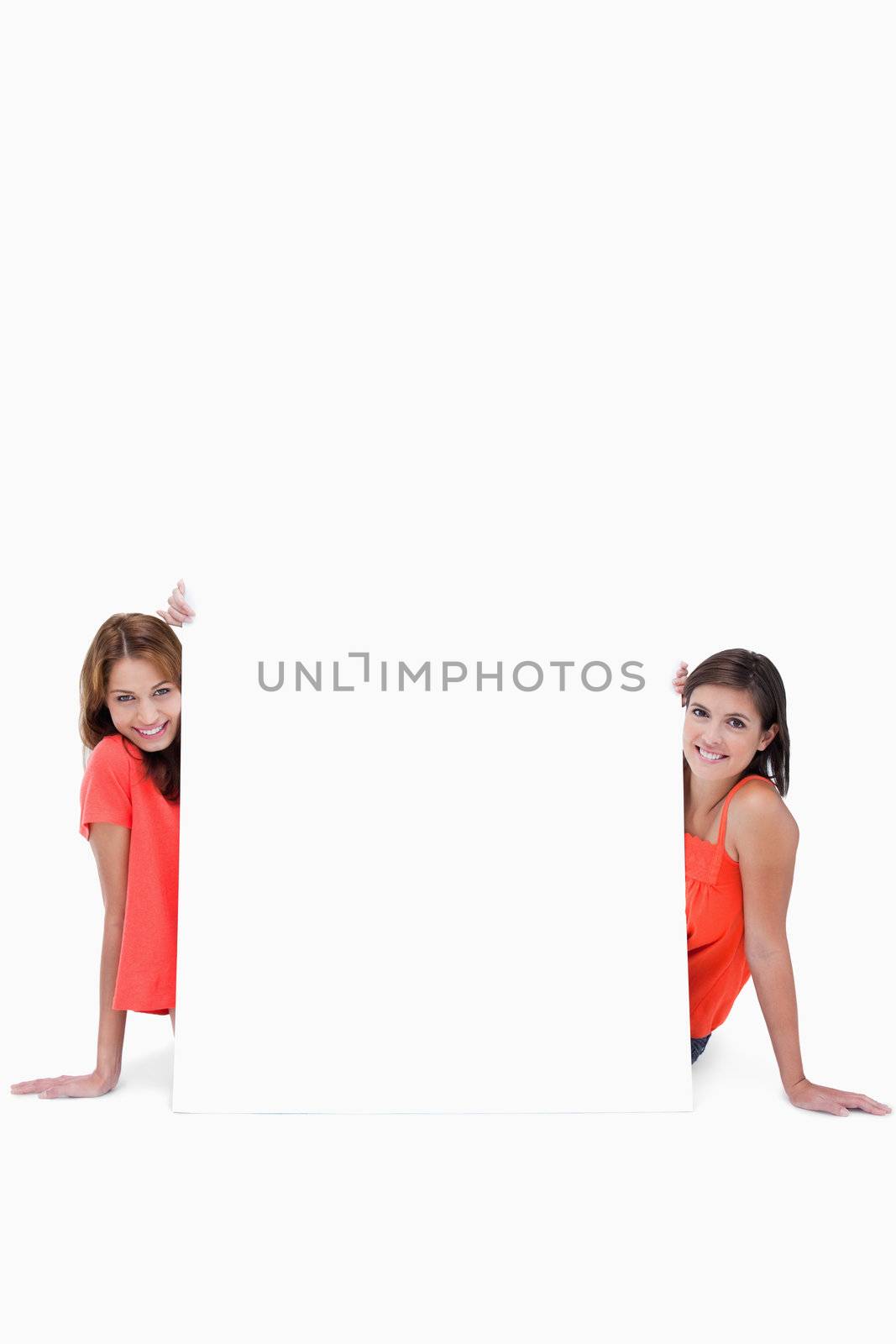 Two smiling teenage girls sitting behind a blank poster by Wavebreakmedia