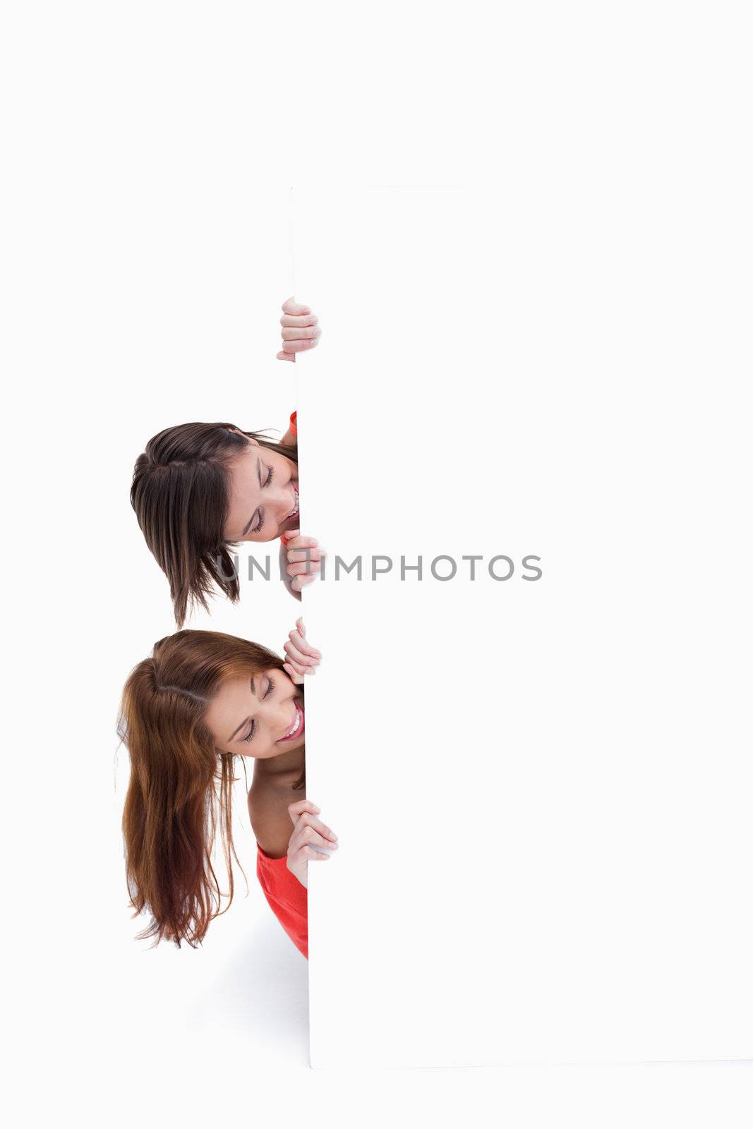 Teenagers hiding behind a blank poster while showing their heads by Wavebreakmedia