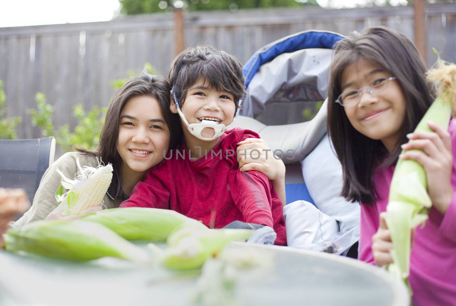 Kids with disabled brother peeling husk off ears of corn