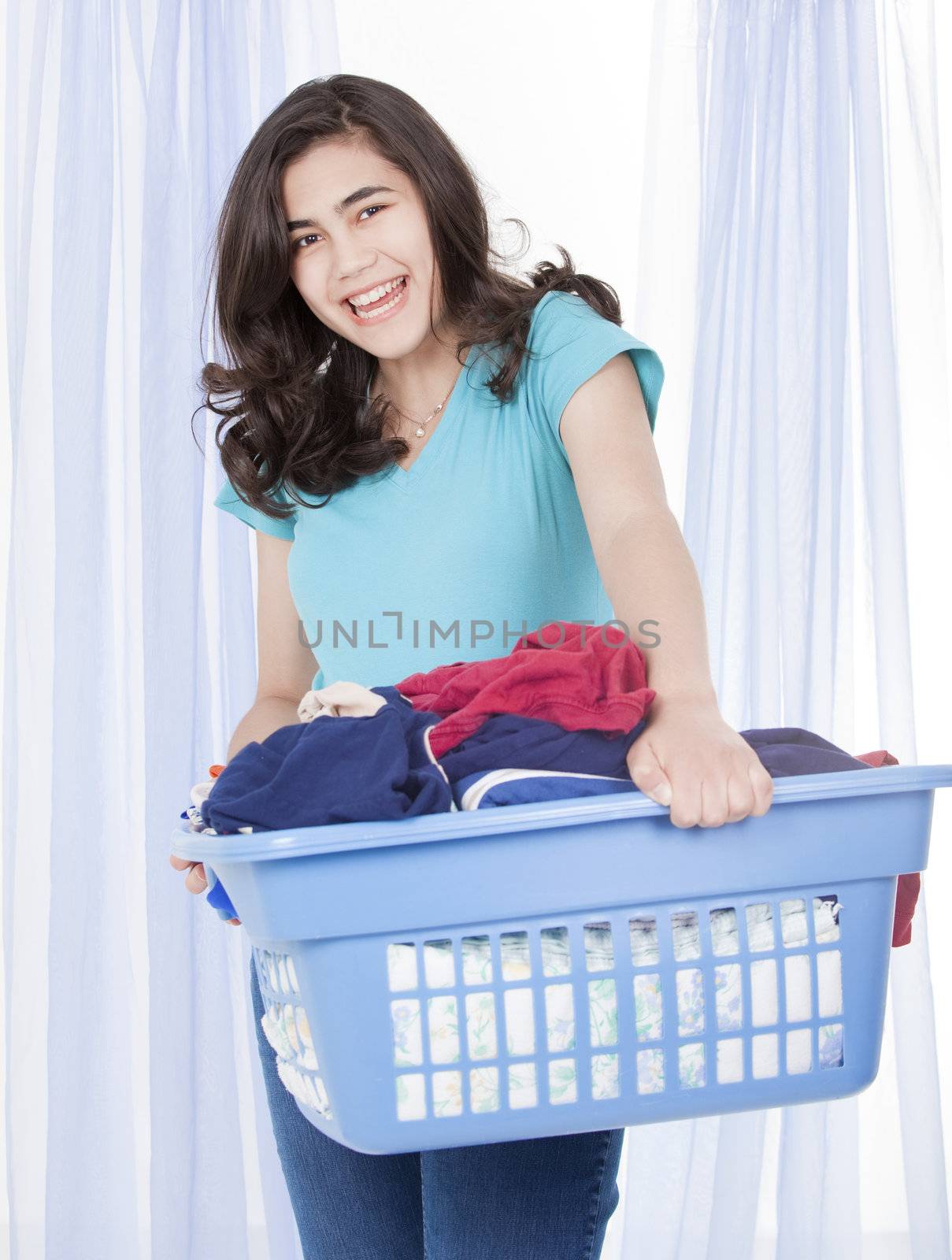 Happy teen girl doing the laundry, carrying a load of clothes in basket