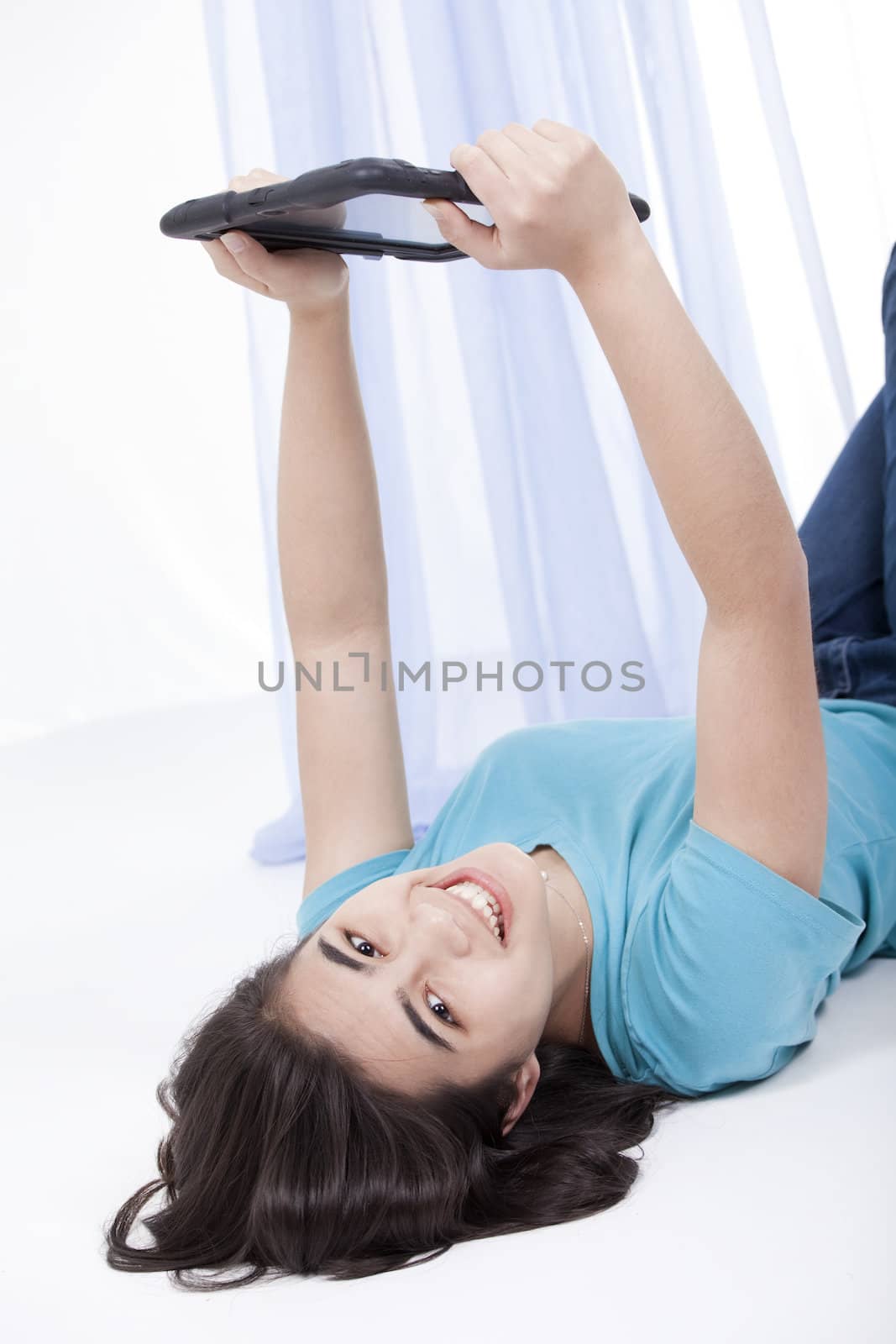 Biracial teen girl holding tablet computer up over head while relaxing on floor 