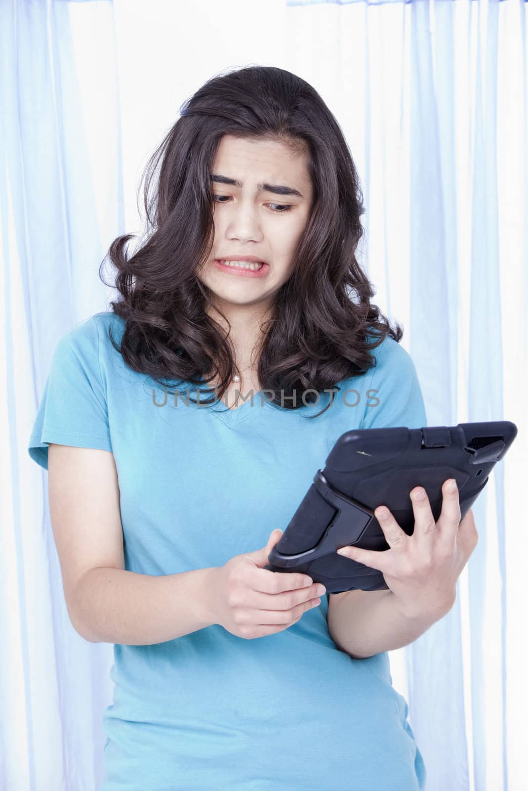 Teen girl looking with disgust or dislike towards computer tablet in hand