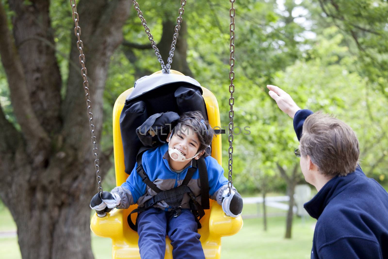 Father pushing disabled son  on yellow handicap swing