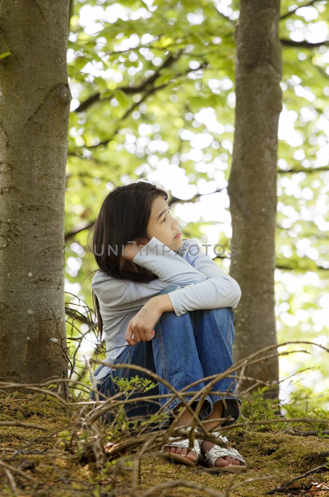 Ten year old girl sitting quietly in woods, looking around thinking