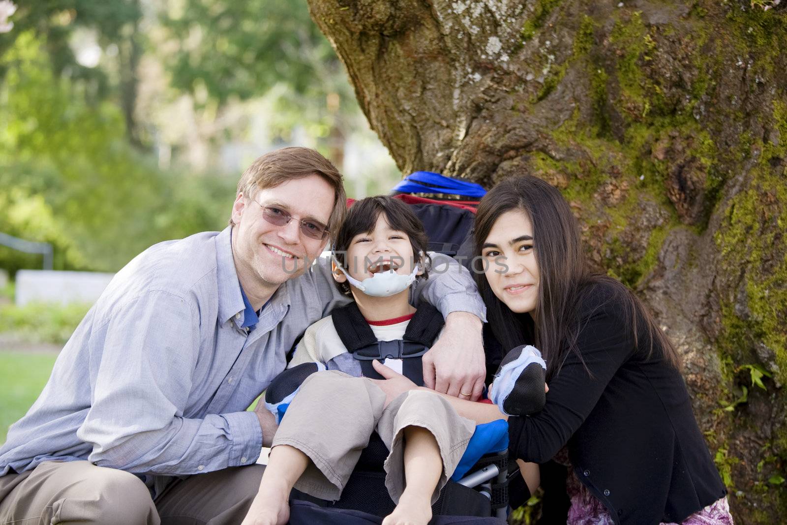 Happy disabled boy with cerebral palsy  in wheelchair surrounded by father and older sister, laughing