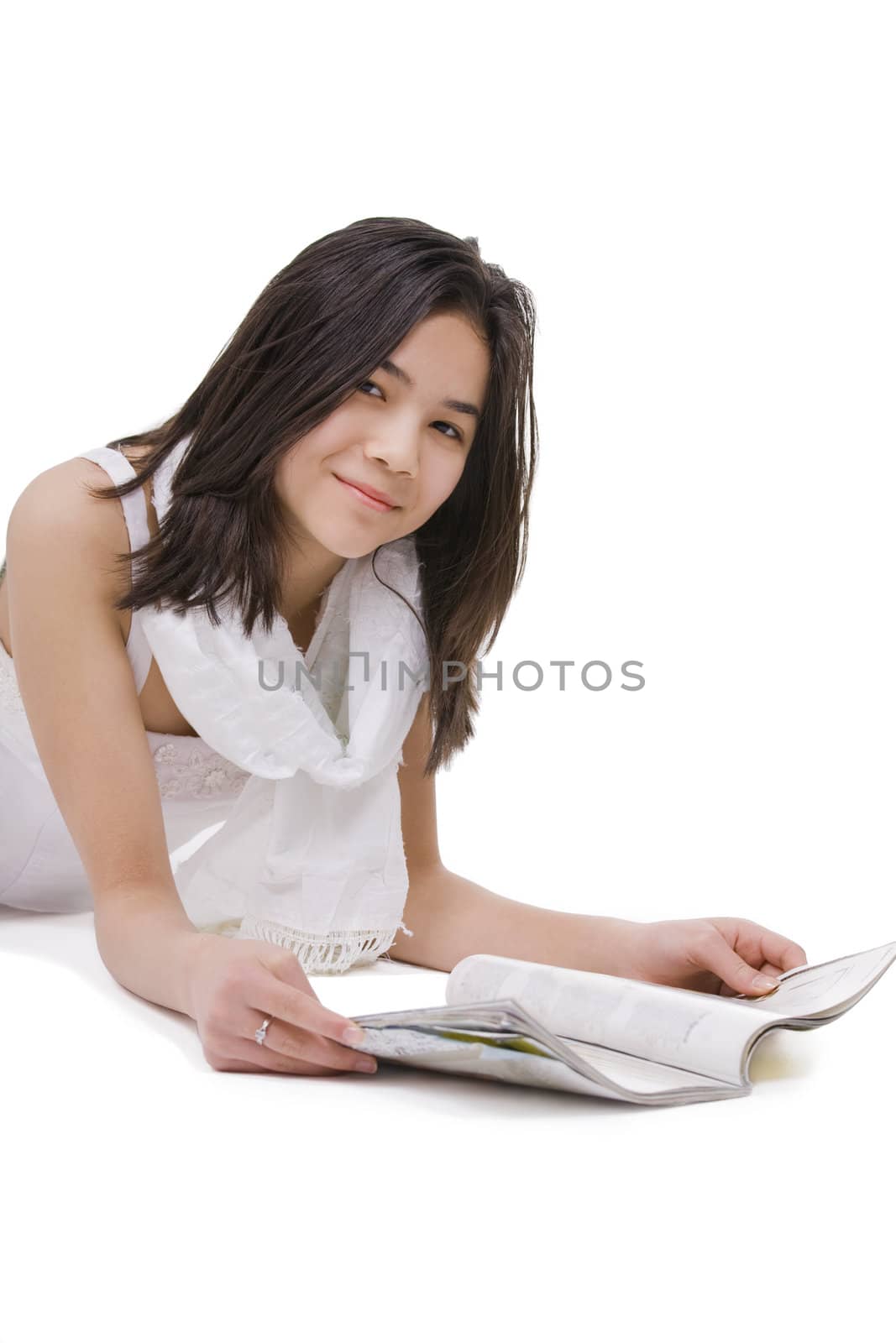 Beautiful young teen girl in white dress or gown lying down reading a magazine, isolated on white