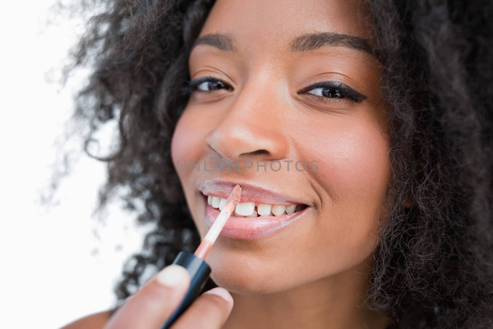 Woman making-up while using a lip gloss applicator against a white background