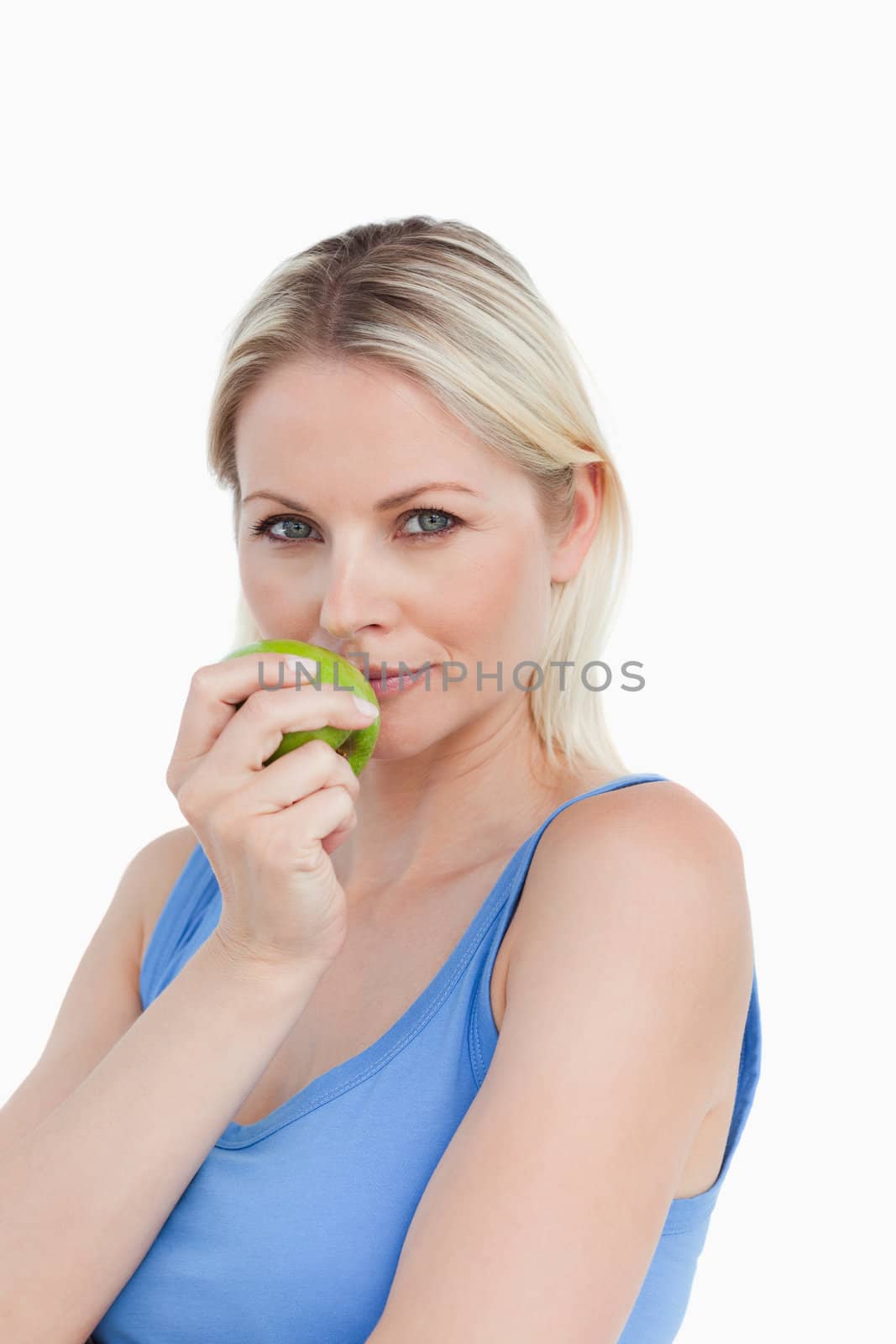 Blonde woman holding an apple close to her mouth against a white background