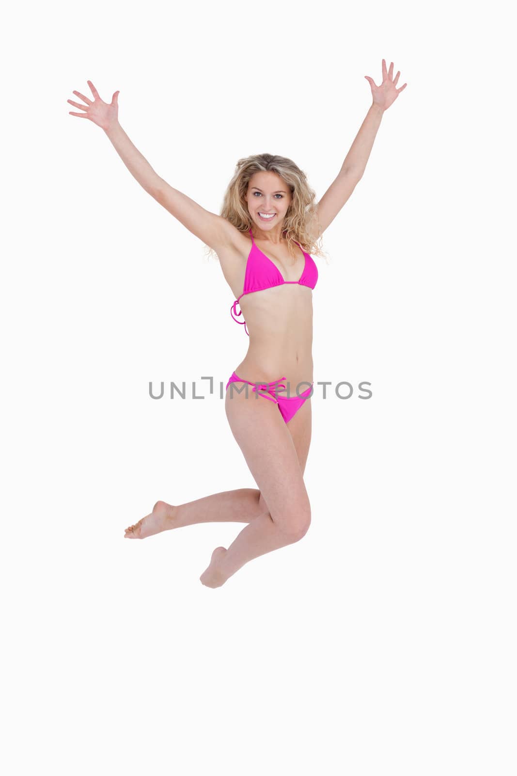 Smiling blonde woman jumping while raising her arms against a white background