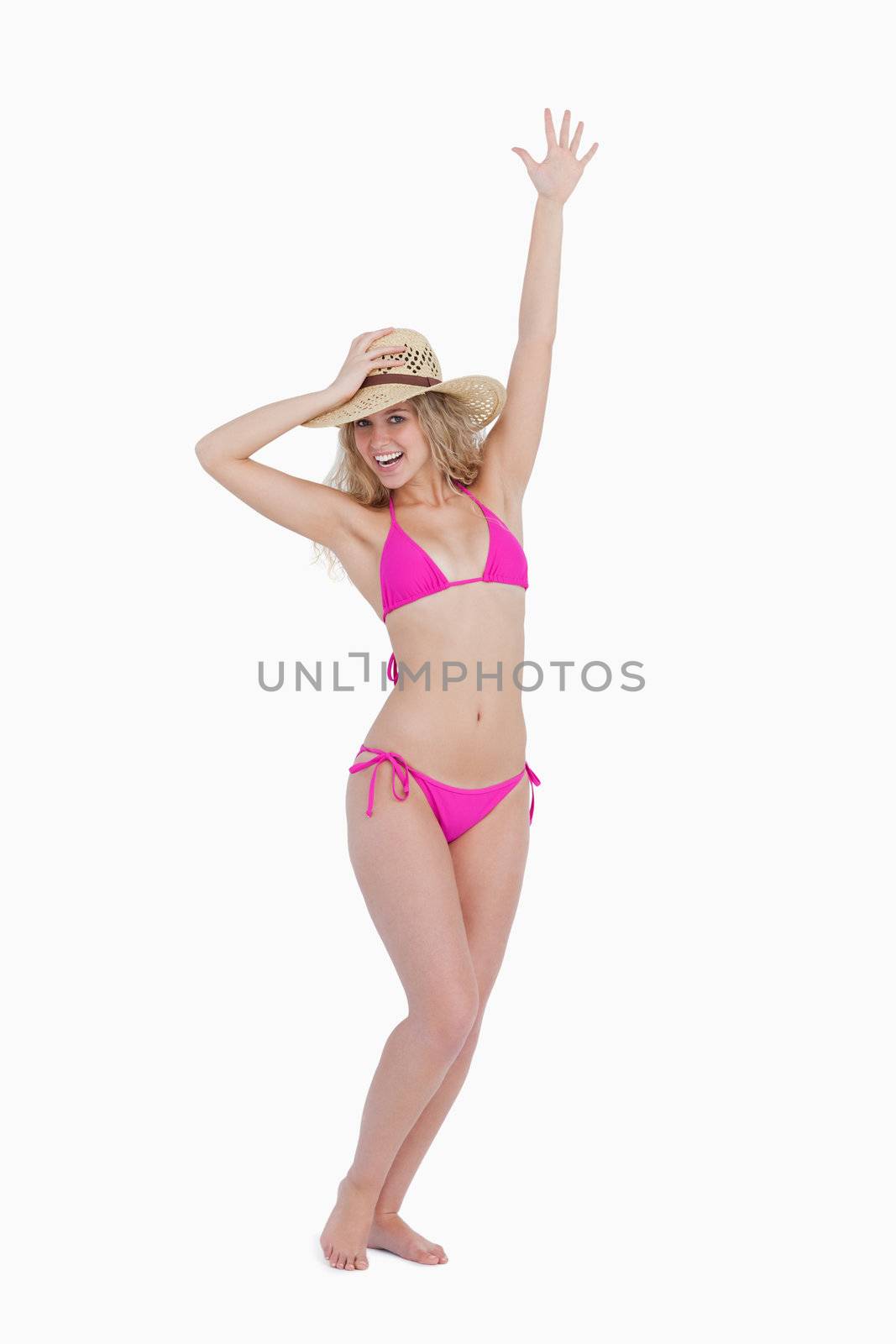 Young woman holding her hat with one arm raised against a white background
