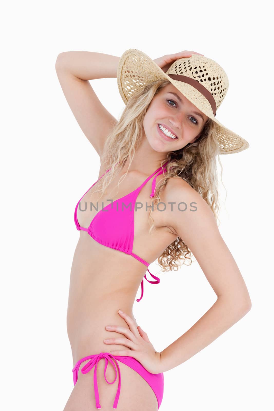 Attractive smiling teenager standing upright with a hand on her hip while holding her hat