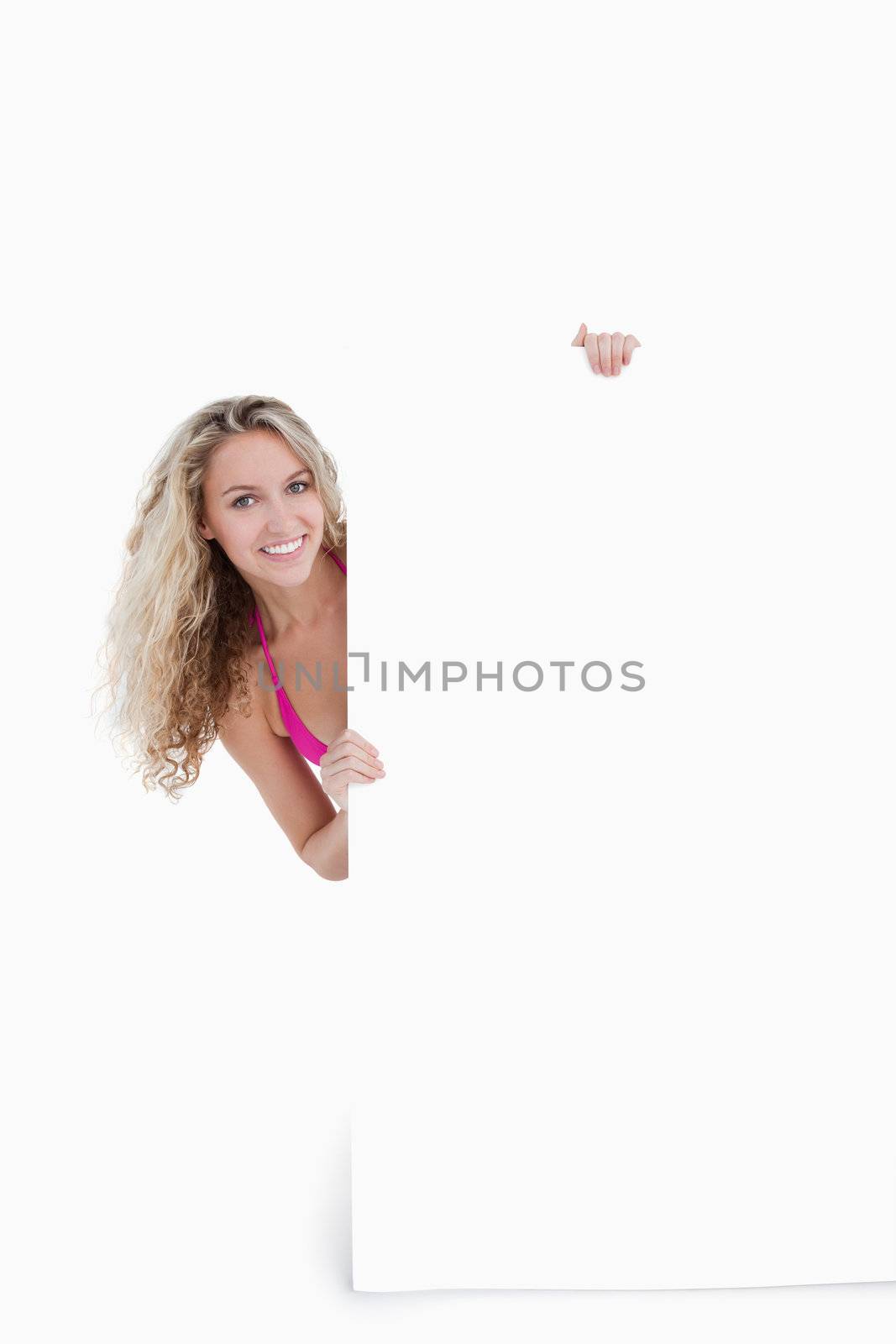 Smiling teenager hiding her body behind a blank poster by Wavebreakmedia