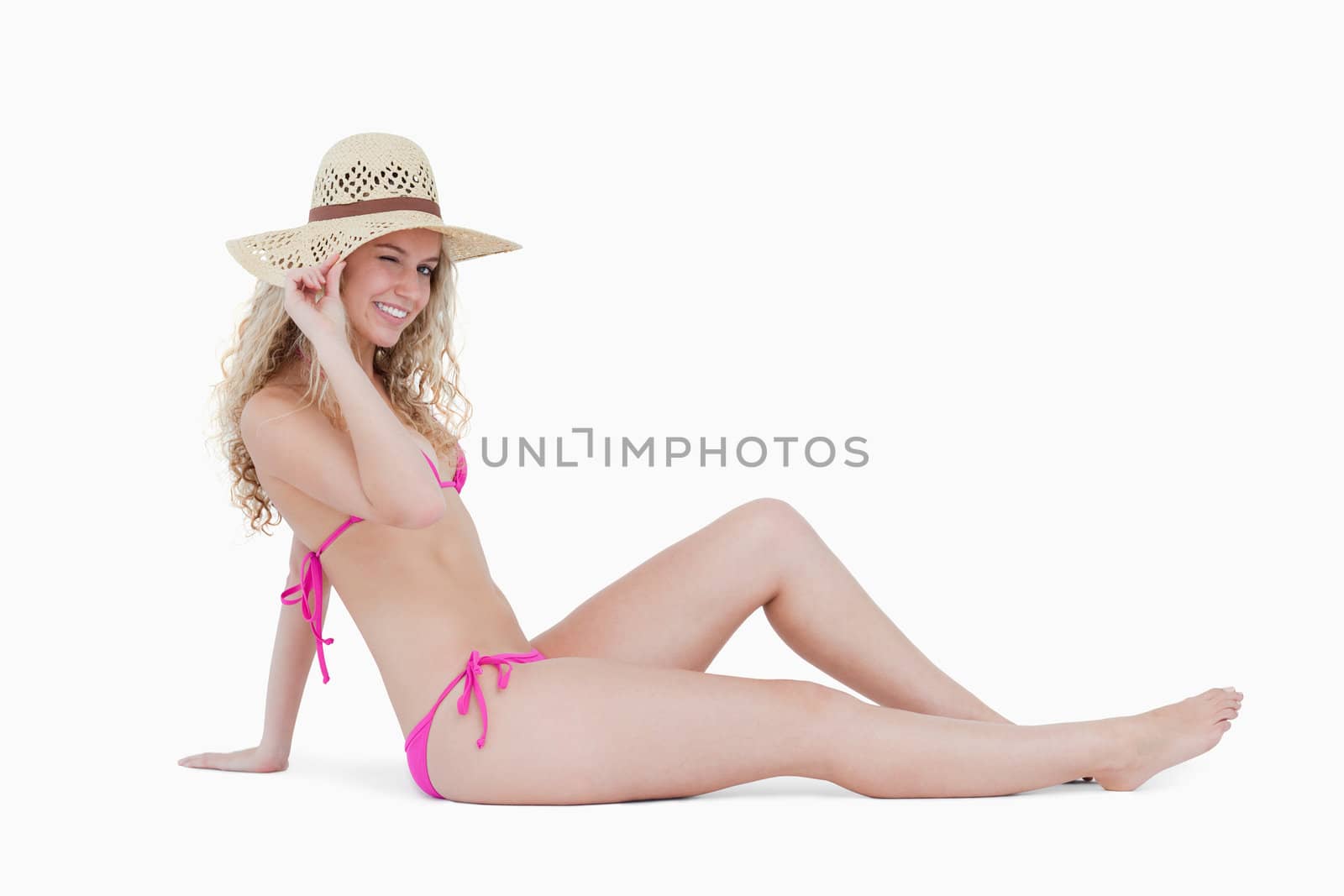 Young woman sitting down while holding her hat brim against a white background