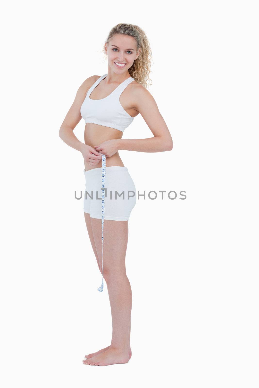 Smiling teenager standing up while measuring her waist by Wavebreakmedia
