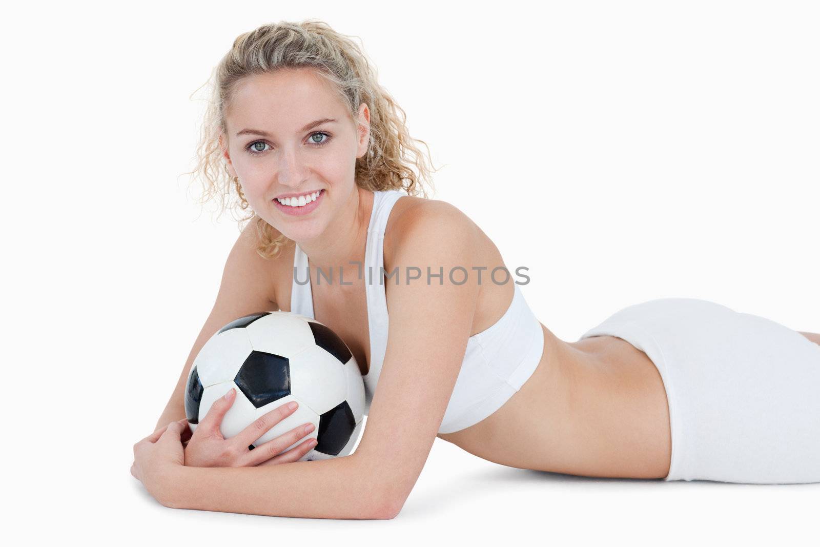 Smiling teenager lying down with a football in her arms against a white background