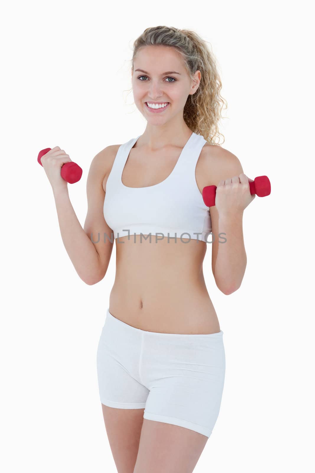 Young attractive woman smiling and lifting red weights against a white background