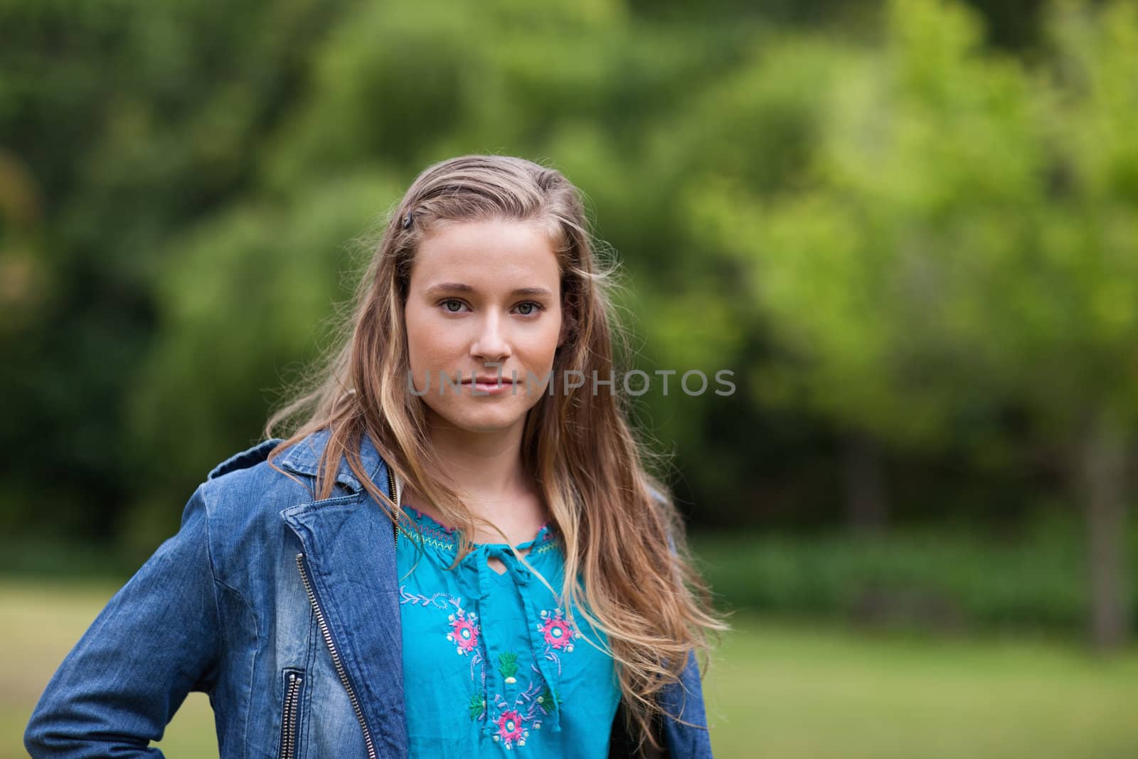 Teenager standing upright in a park while looking ahead seriously
