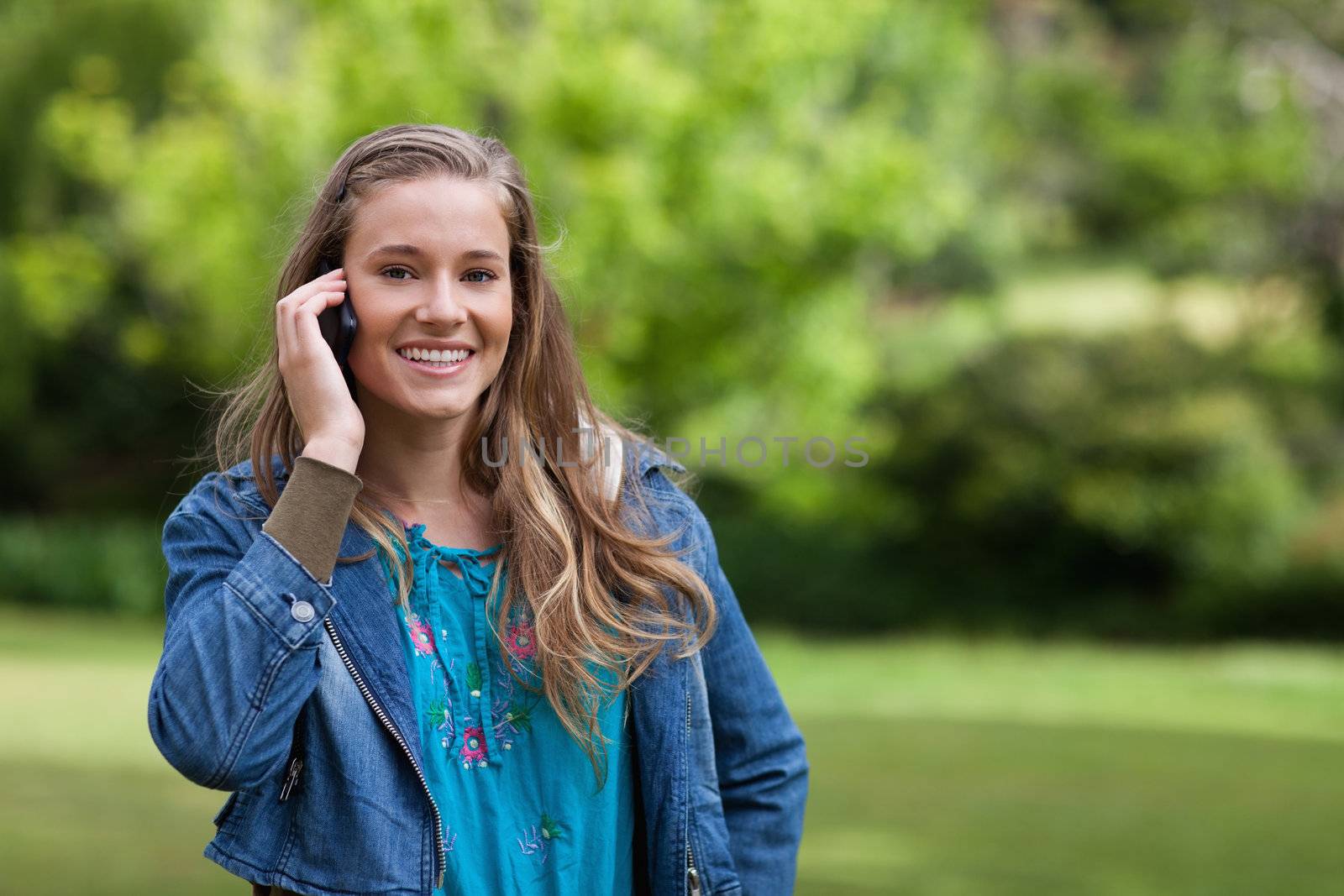 Young smiling girl talking on the phone while standing in a park by Wavebreakmedia