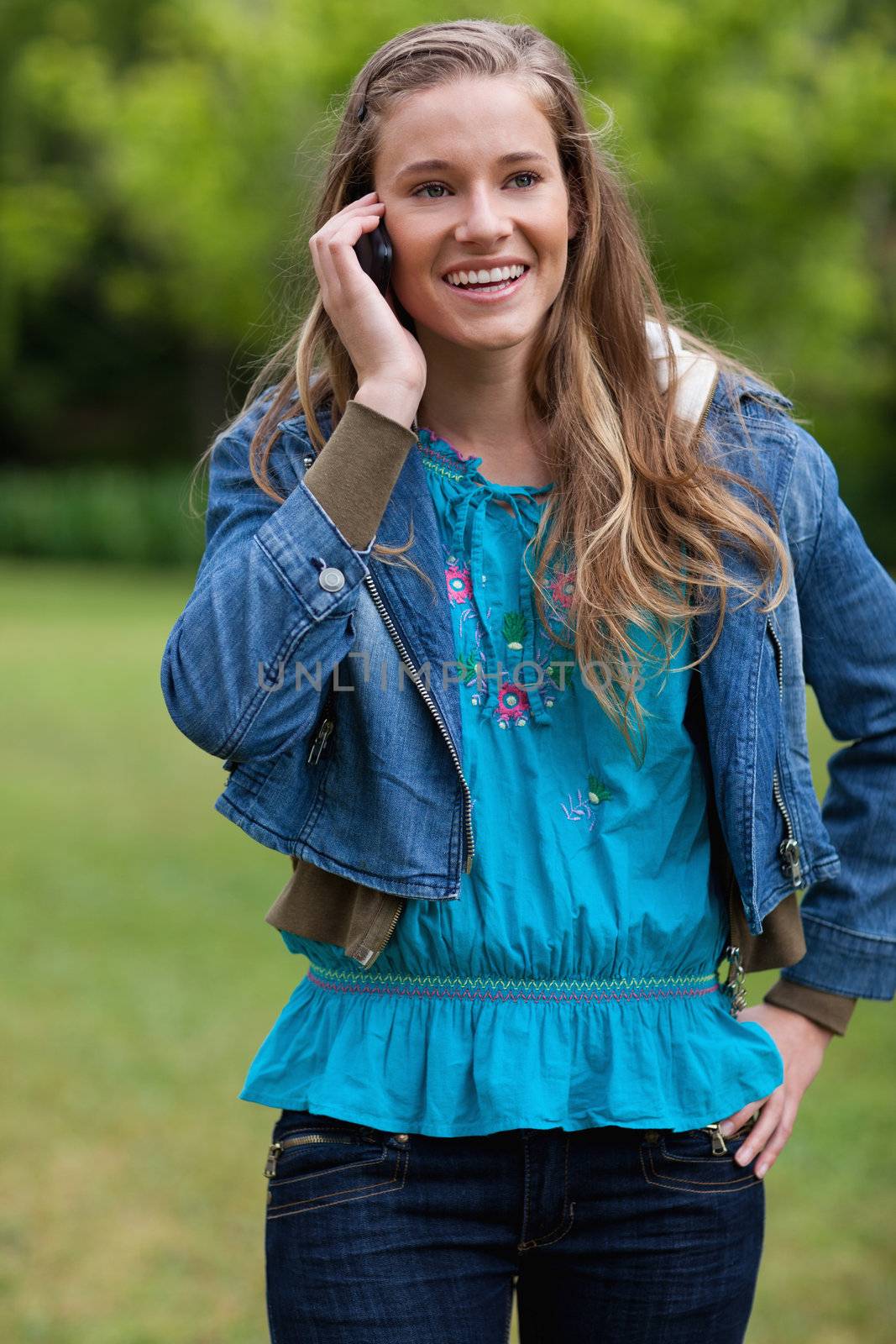 Smiling teenage girl talking on the phone while standing in a pa by Wavebreakmedia