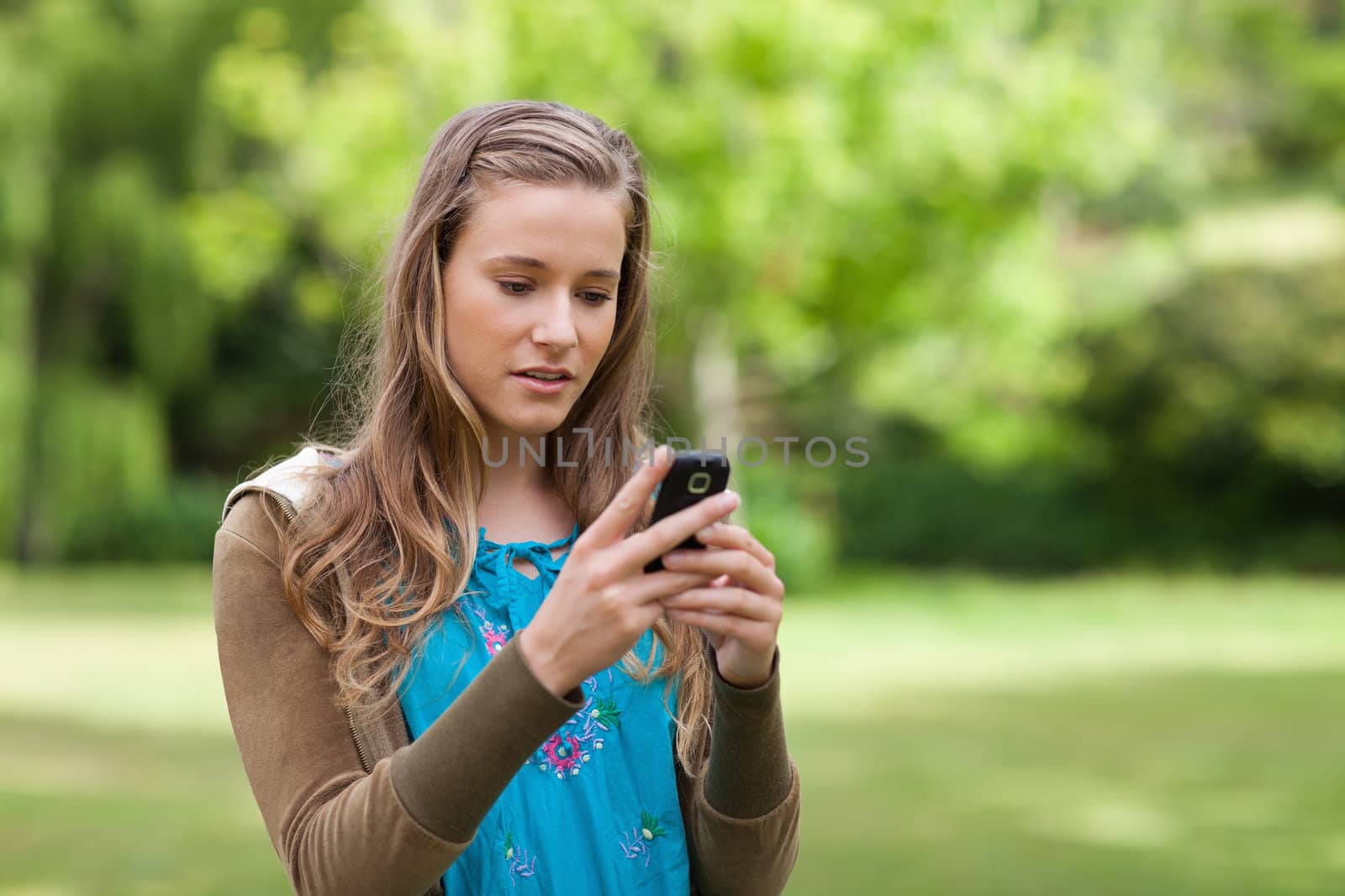 Serious teenager sending a text with her cellphone while standing in a park