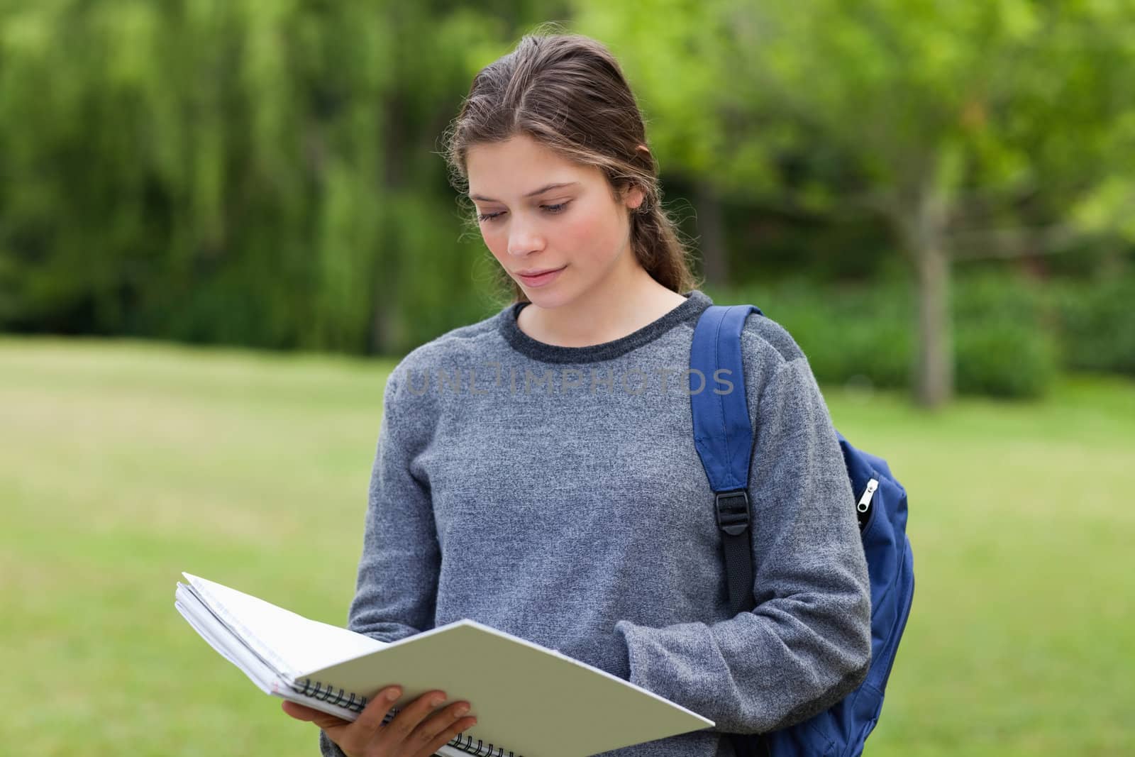 Young serious woman reading her notebook while standing in a par by Wavebreakmedia
