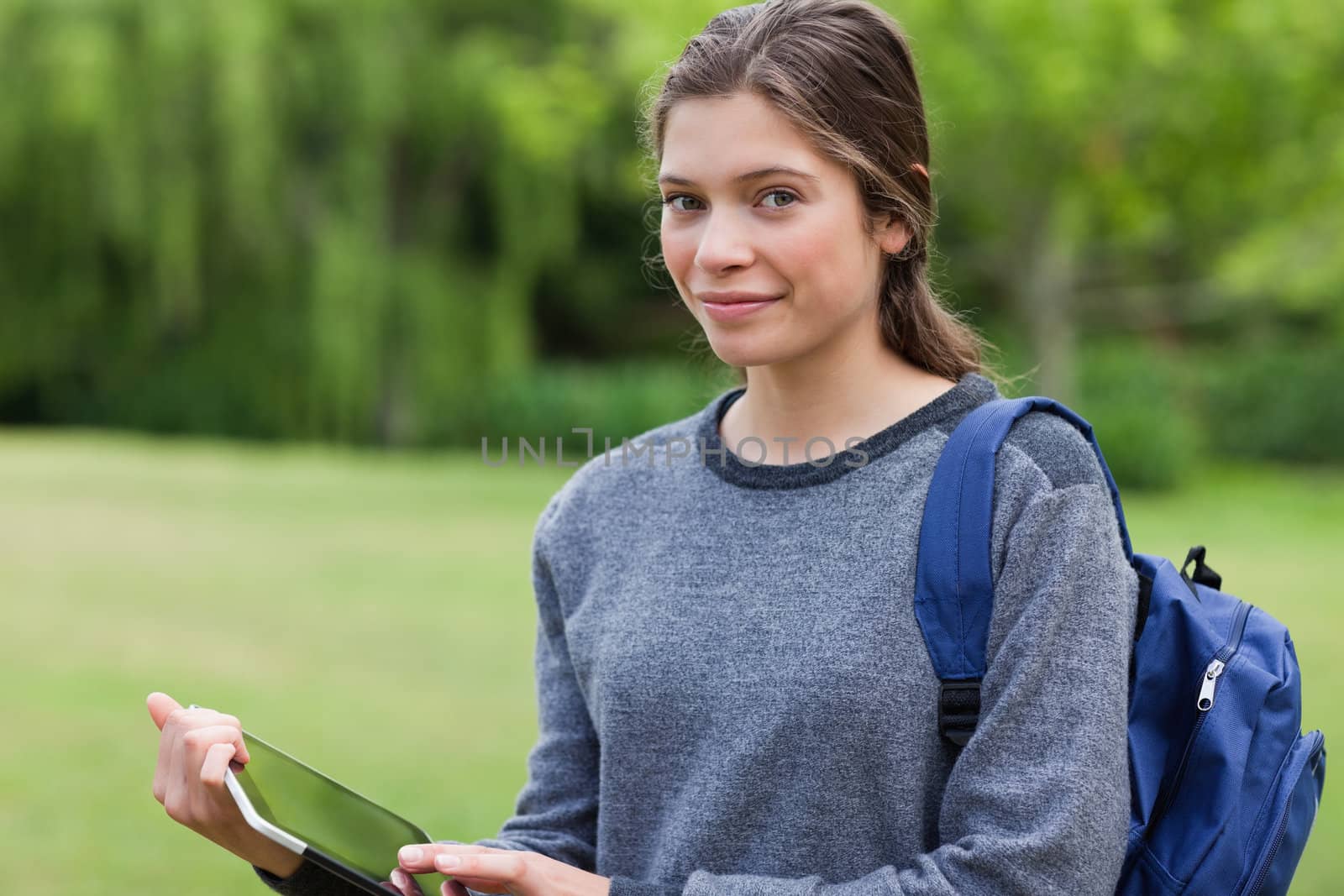 Smiling young woman holding a tablet pc while standing in a park by Wavebreakmedia