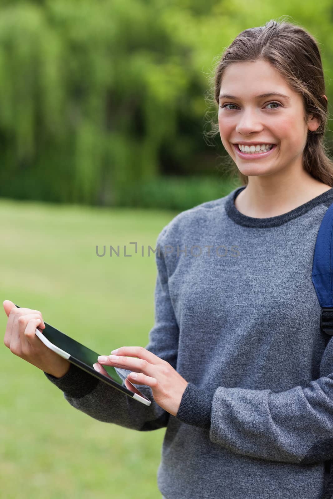 Young smiling girl using her tablet computer while standing upright in a park